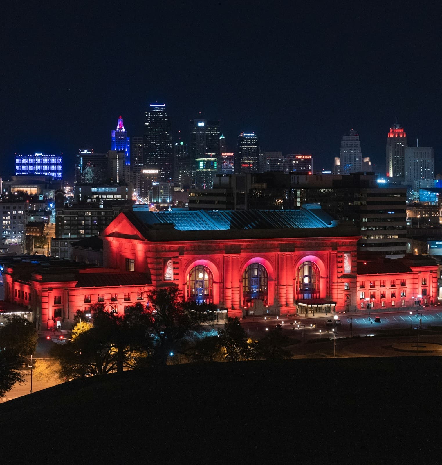 A view of Union Station lit up in red LED lighting in front of a view of the city skyline at nighttime.