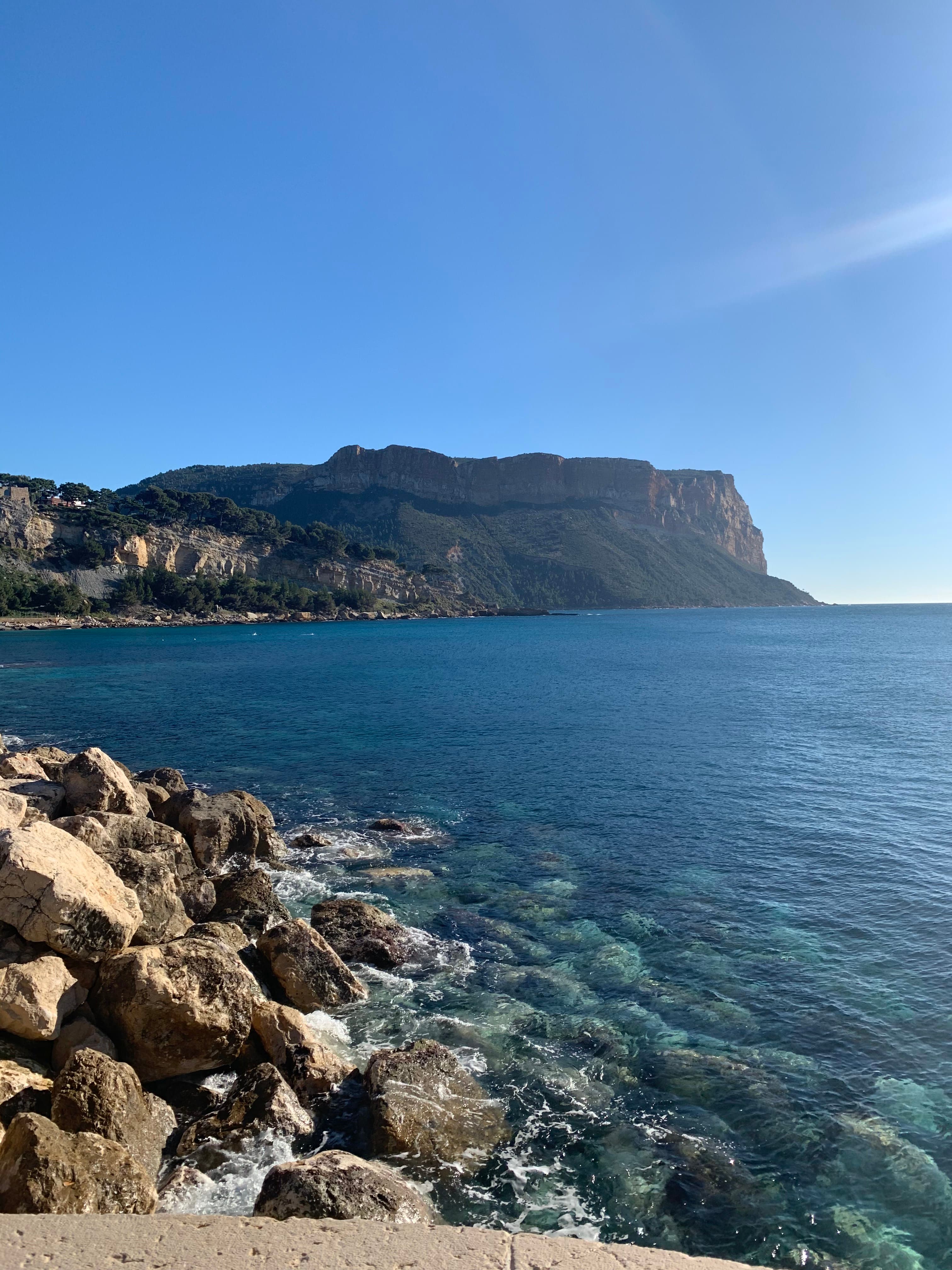 Cassis beach with a rocky shore and sea cliffs in the distance.