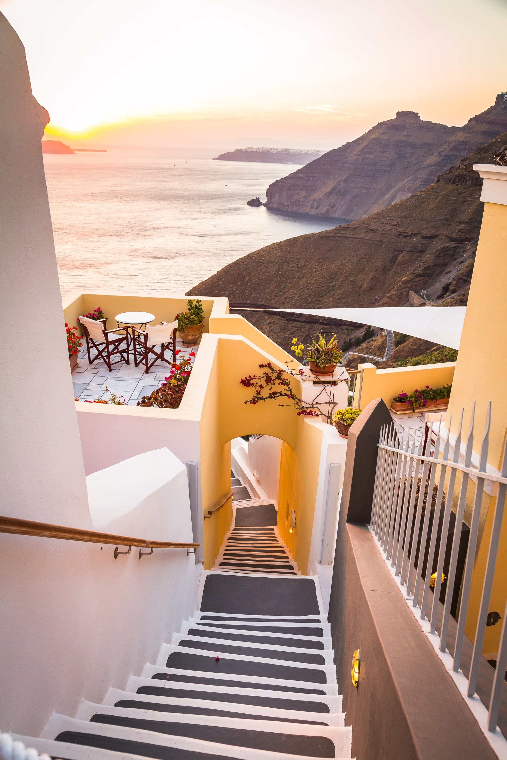 A white-washed staircase flanked by buildings in front of the Mediterranean in Greece.