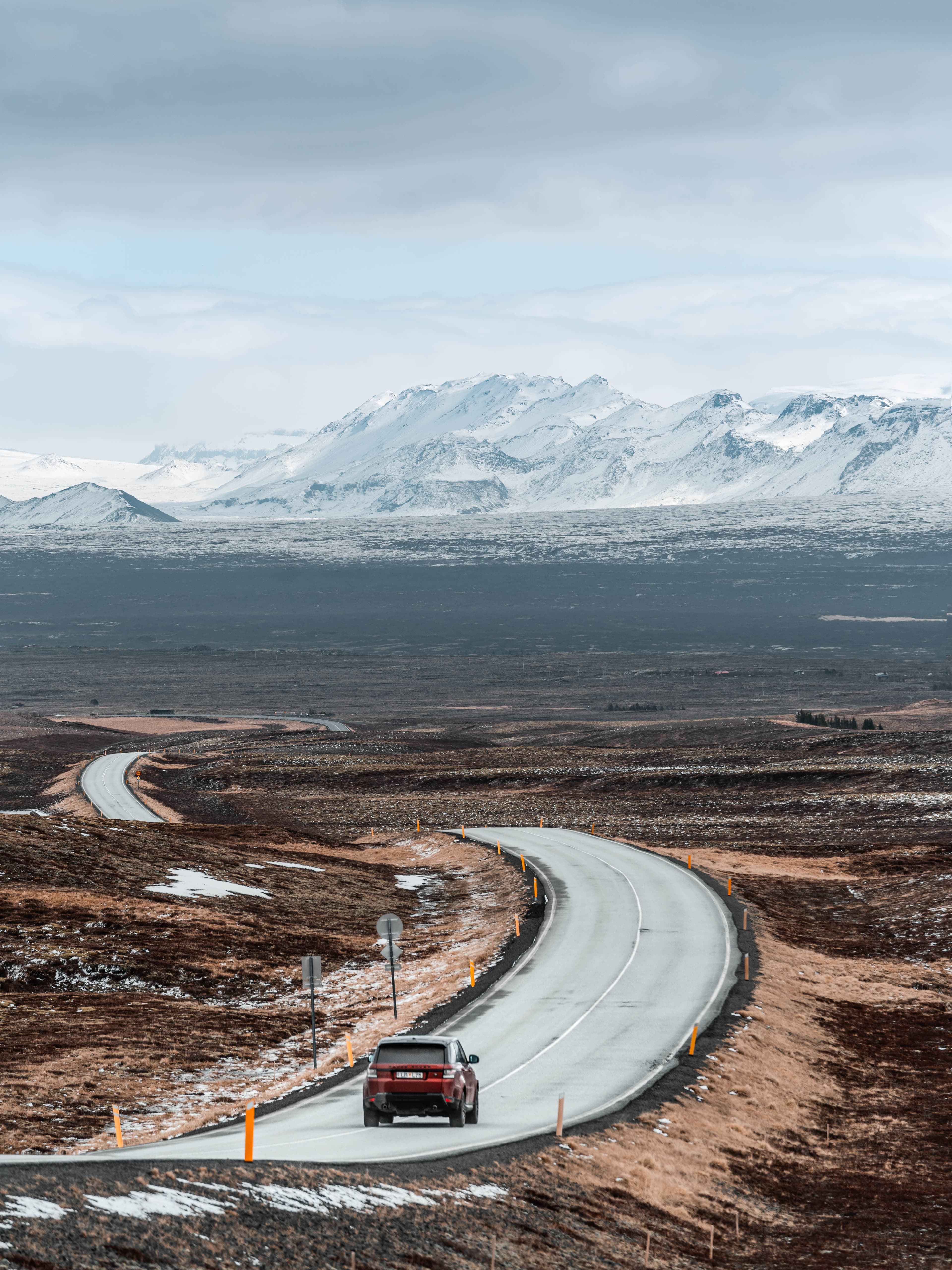 Car driving on winding road with mountains in the background and clouds in the sky