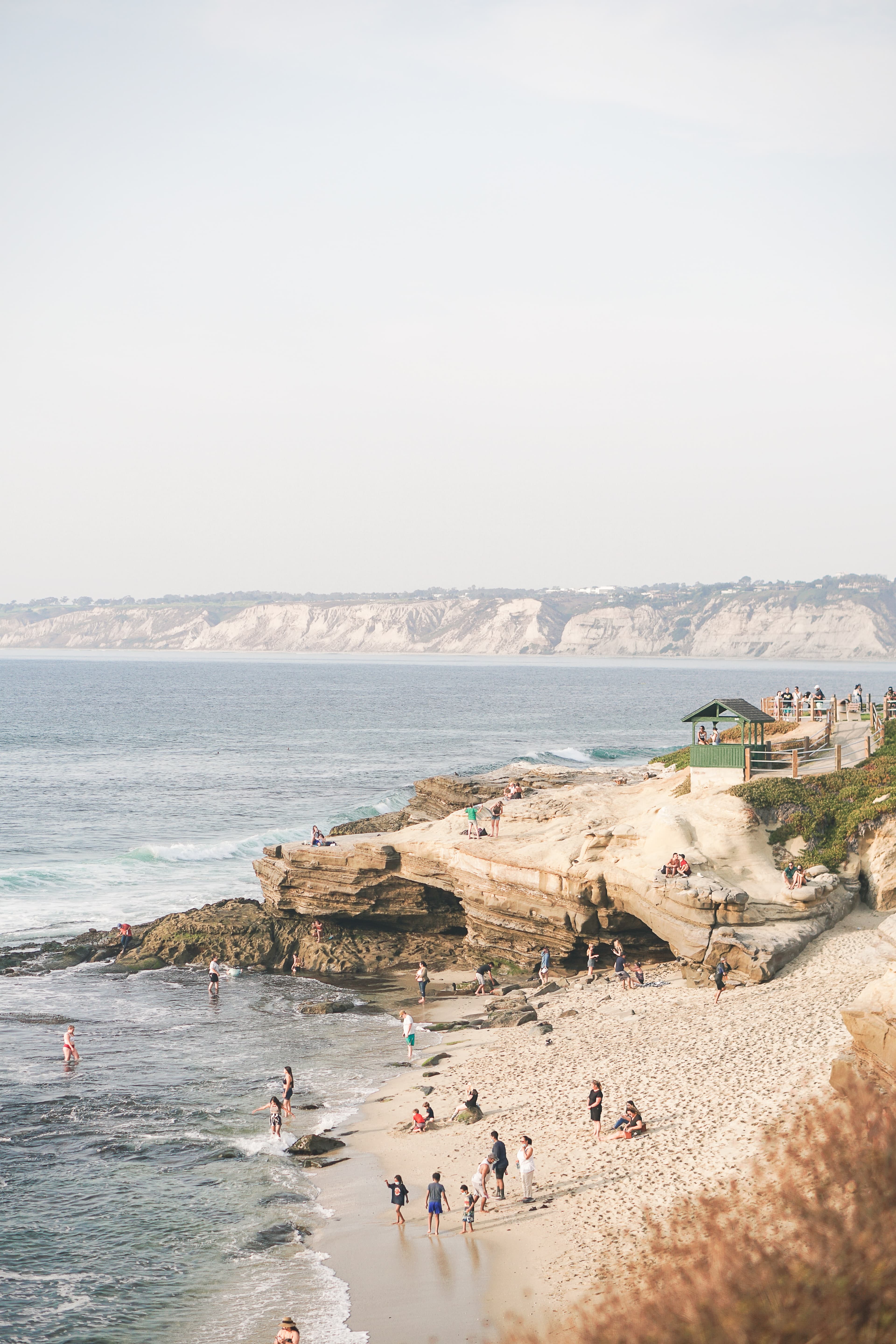 People stand on the sand and in the water on La Jolla Cove in San Diego