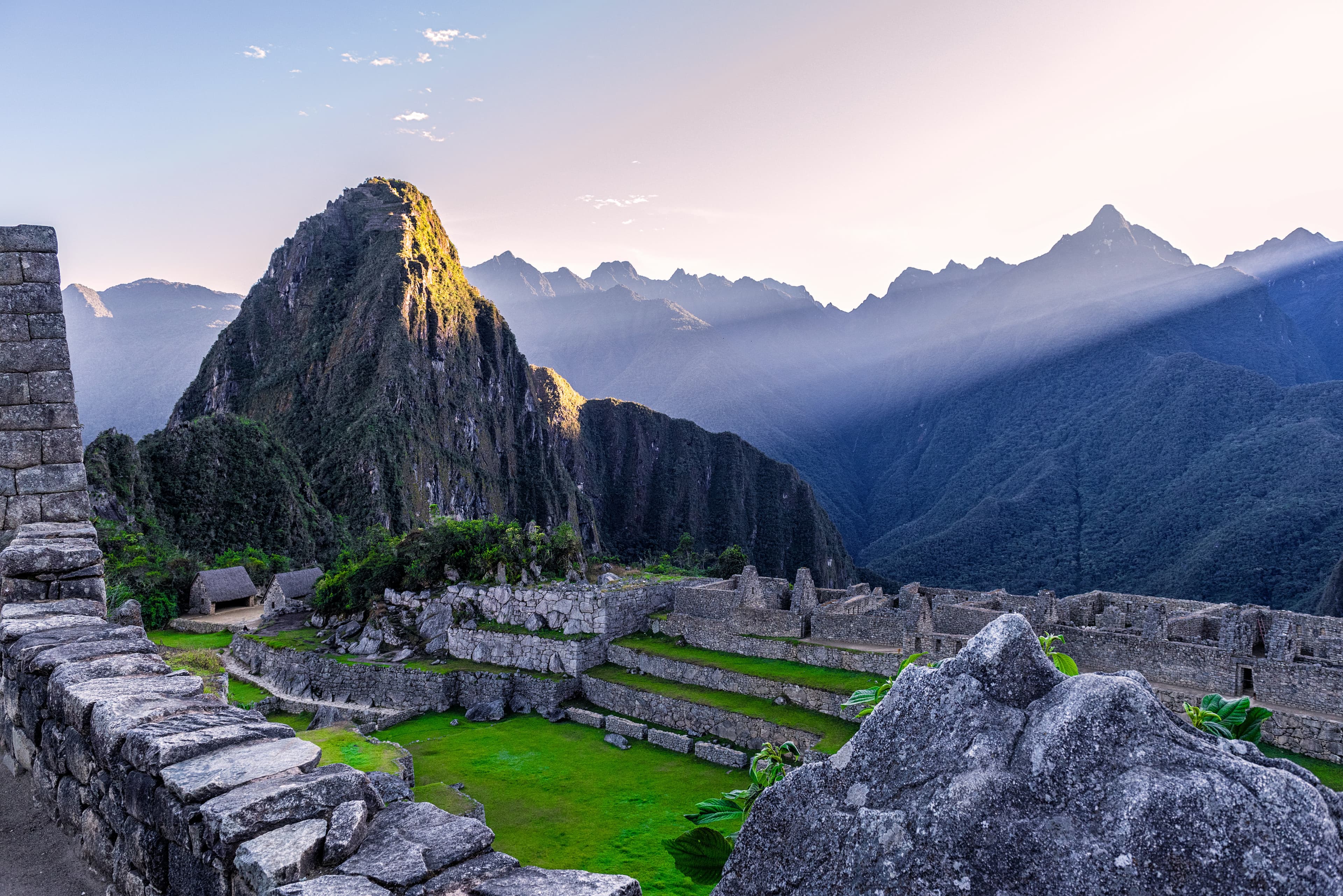 Machu Picchu in Peru green grass with grey stones and blue mountains with a beaming light