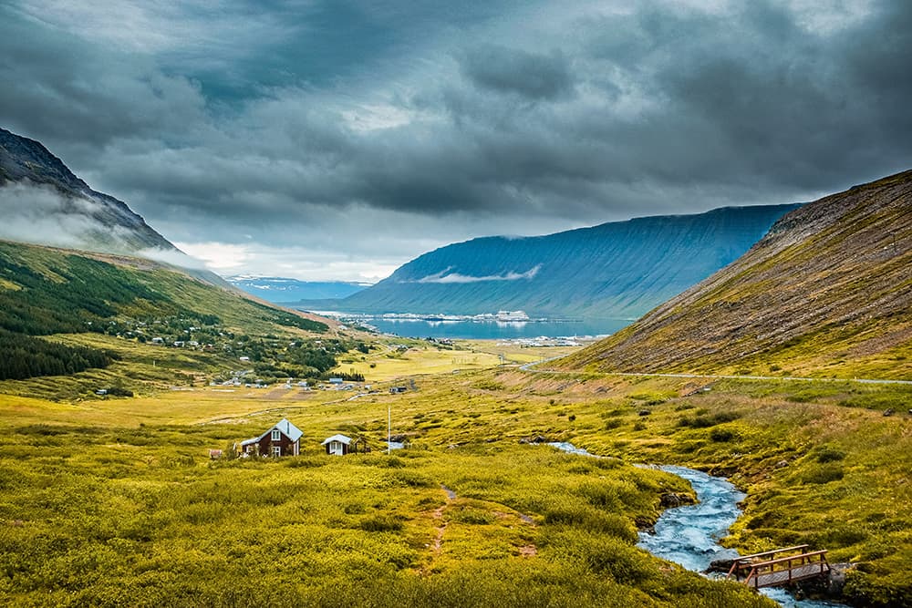 A skyline view of mountains in the Westfjords, Iceland with small houses in the central valley.