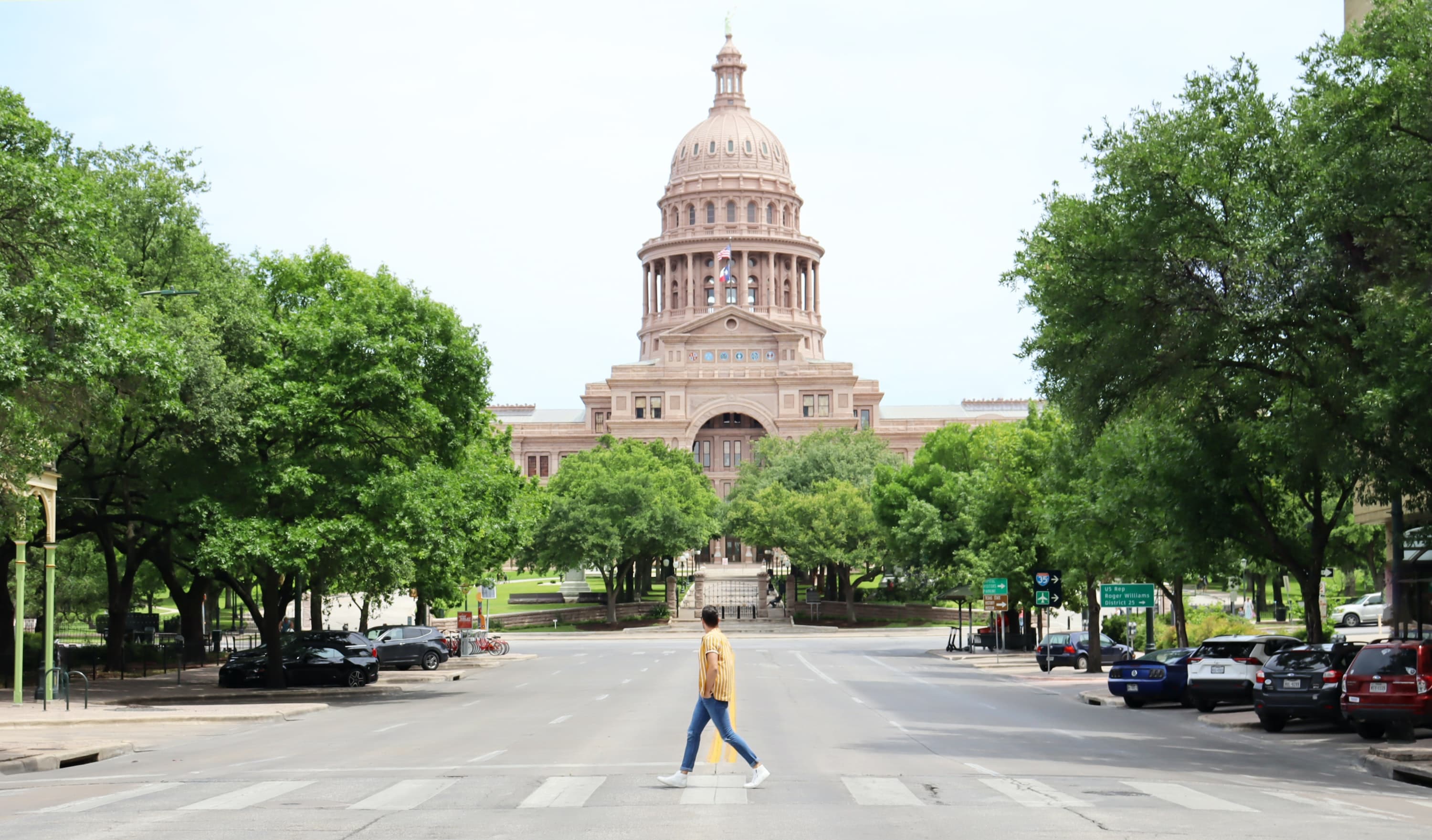 Man walks in crosswalk with capitol building in the back in Austin, Texas
