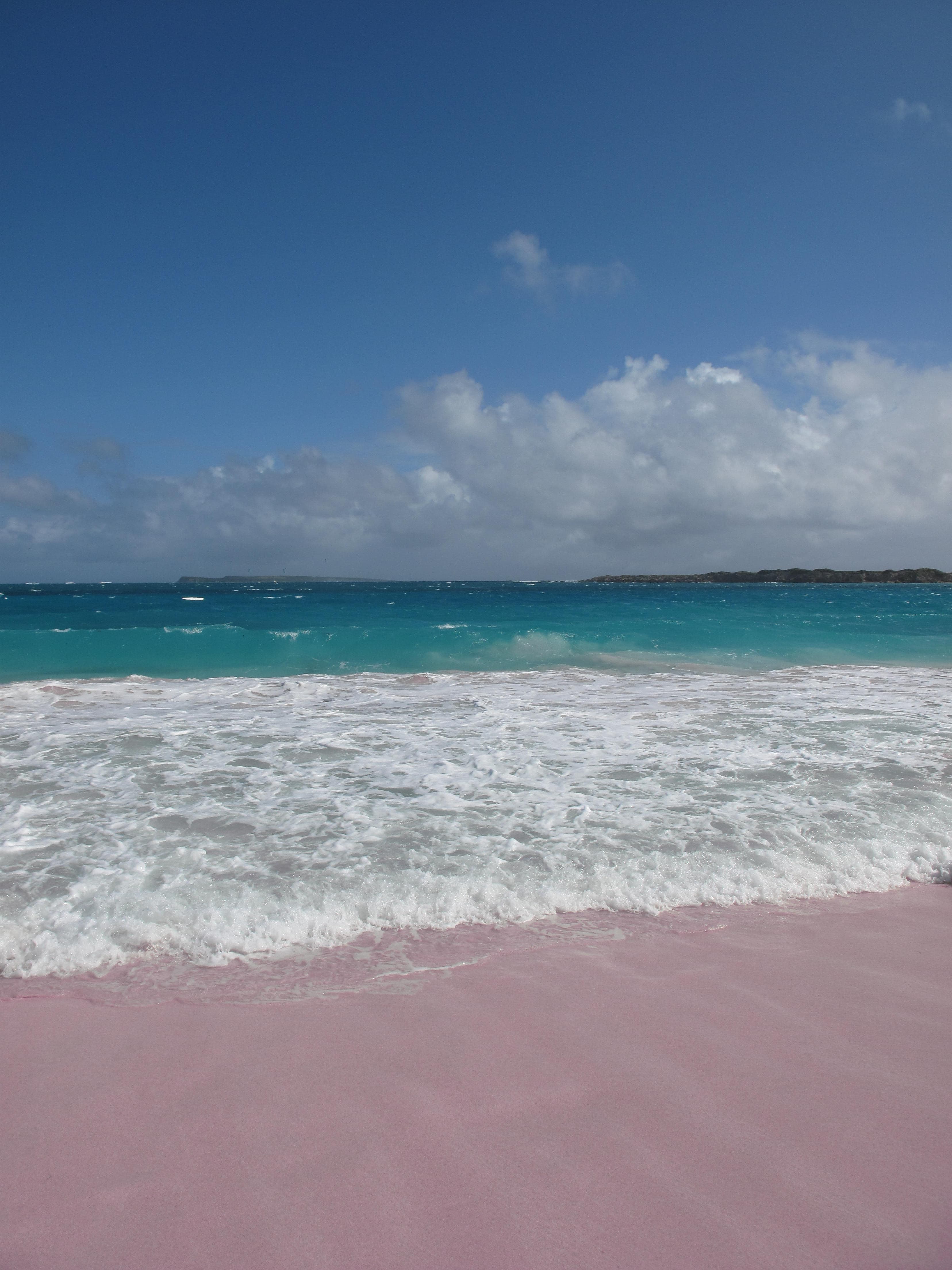 Blue water with white waves crashing onto pink sand in St. Martin in the Caribbean.