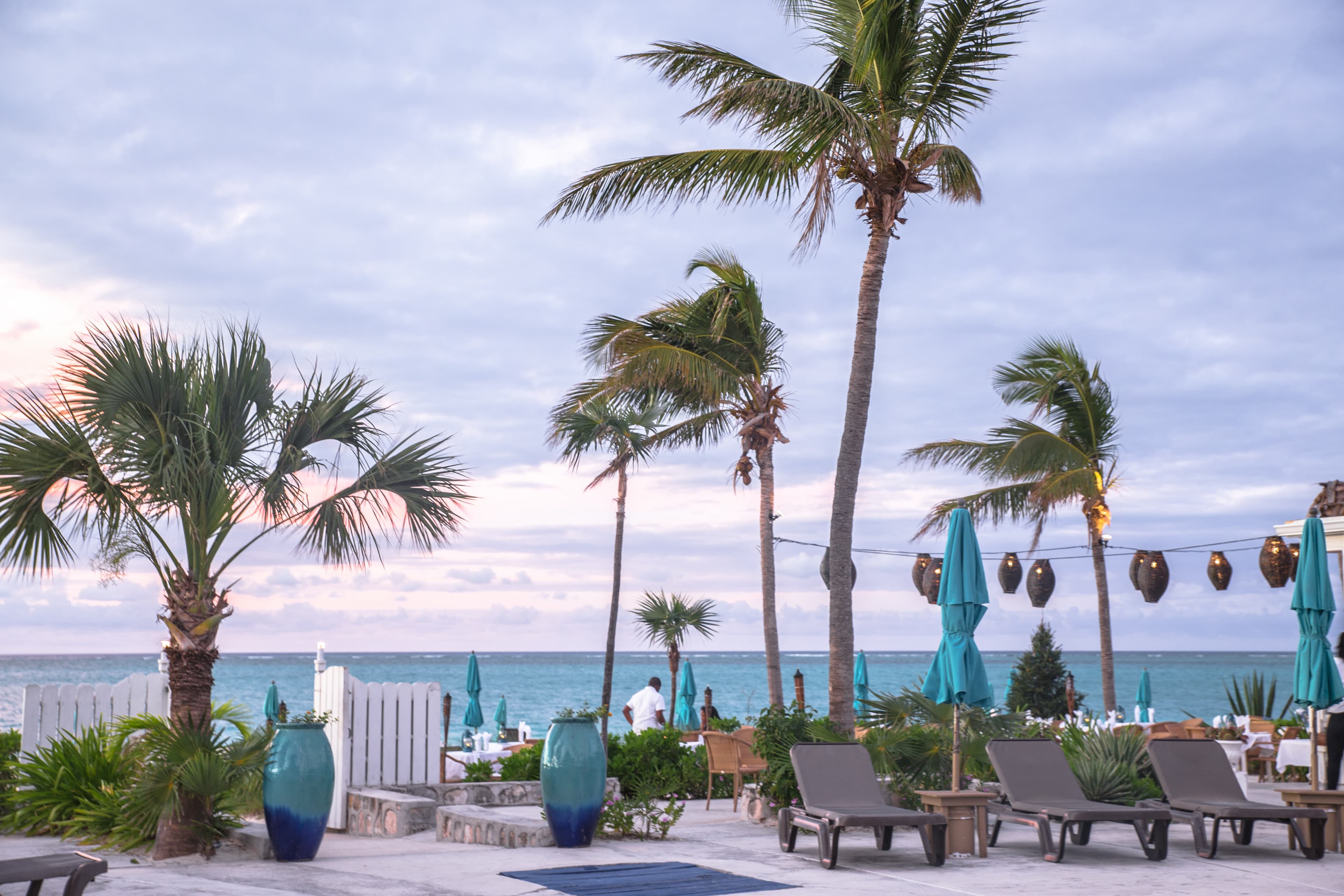 Lounge chairs and palm trees next to a body of water with clouds in the sky