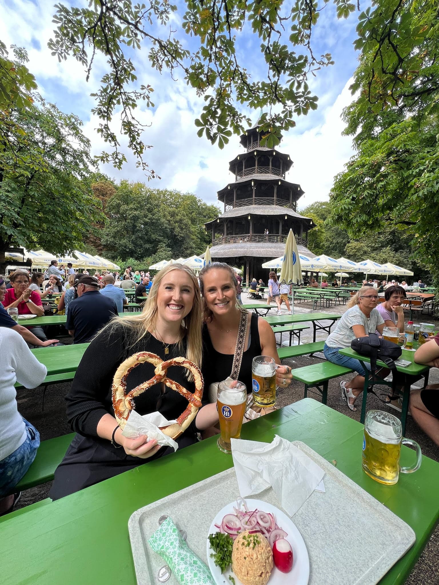 Two people posing for a photo at a green table with big pretzels and glasses of beer
