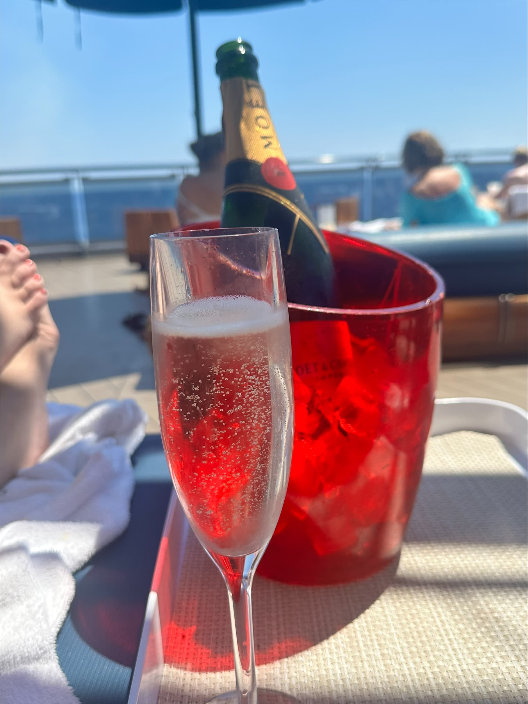 A red ice bucket containing a champagne bottle and a champagne flute sitting on a table