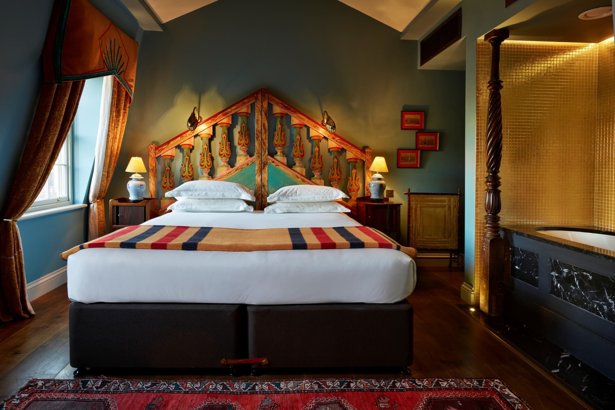 a plush bed in a fancy hotel room with teal walls and a dark-wood floor