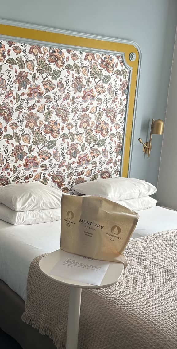 A hotel room bedroom with a flora-decorated wall behind the made bed