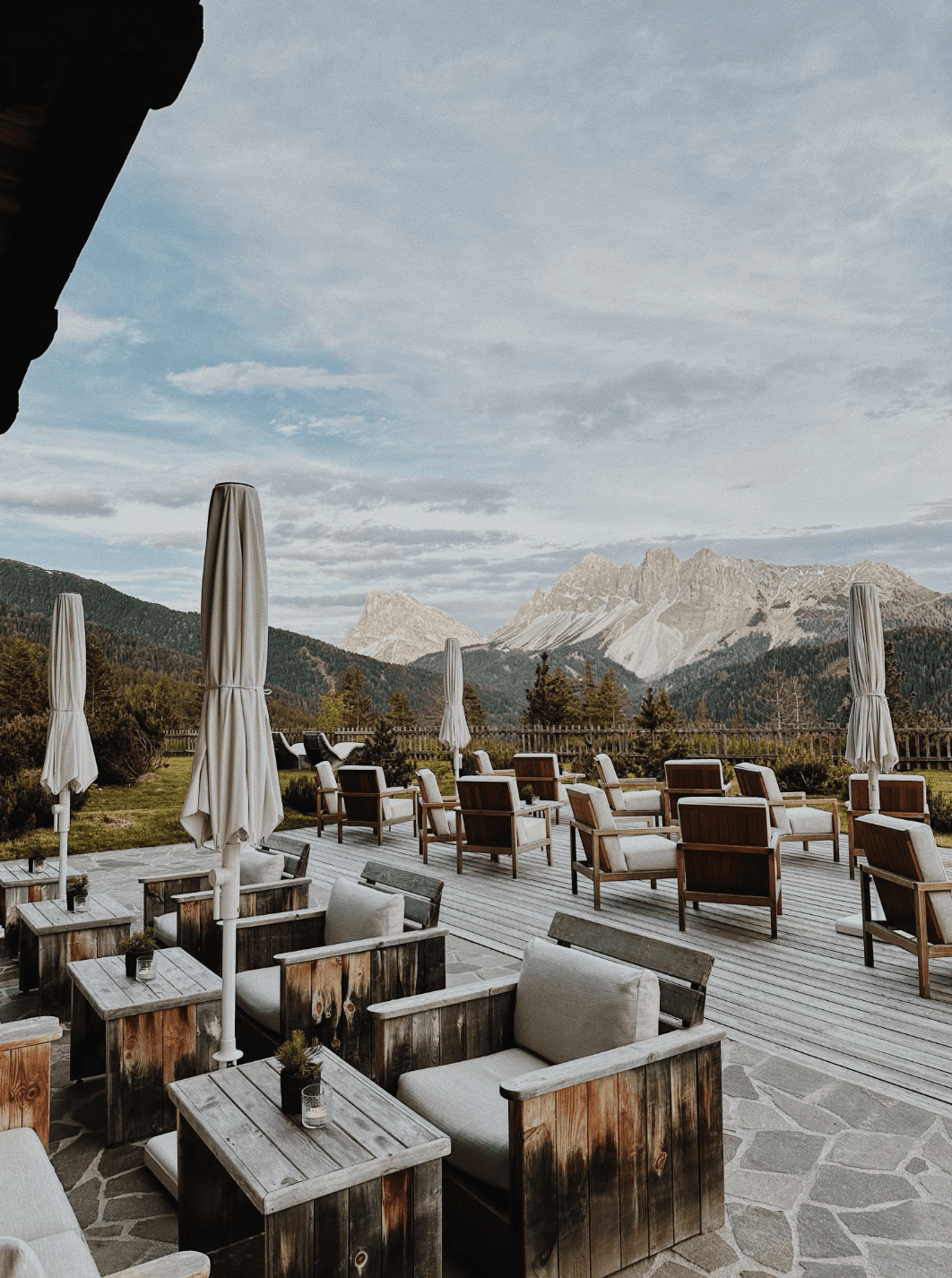 Outdoor dining with comfy chairs and umbrellas lining the patio overlooking the snow-capped mountains and misty afternoon sky.