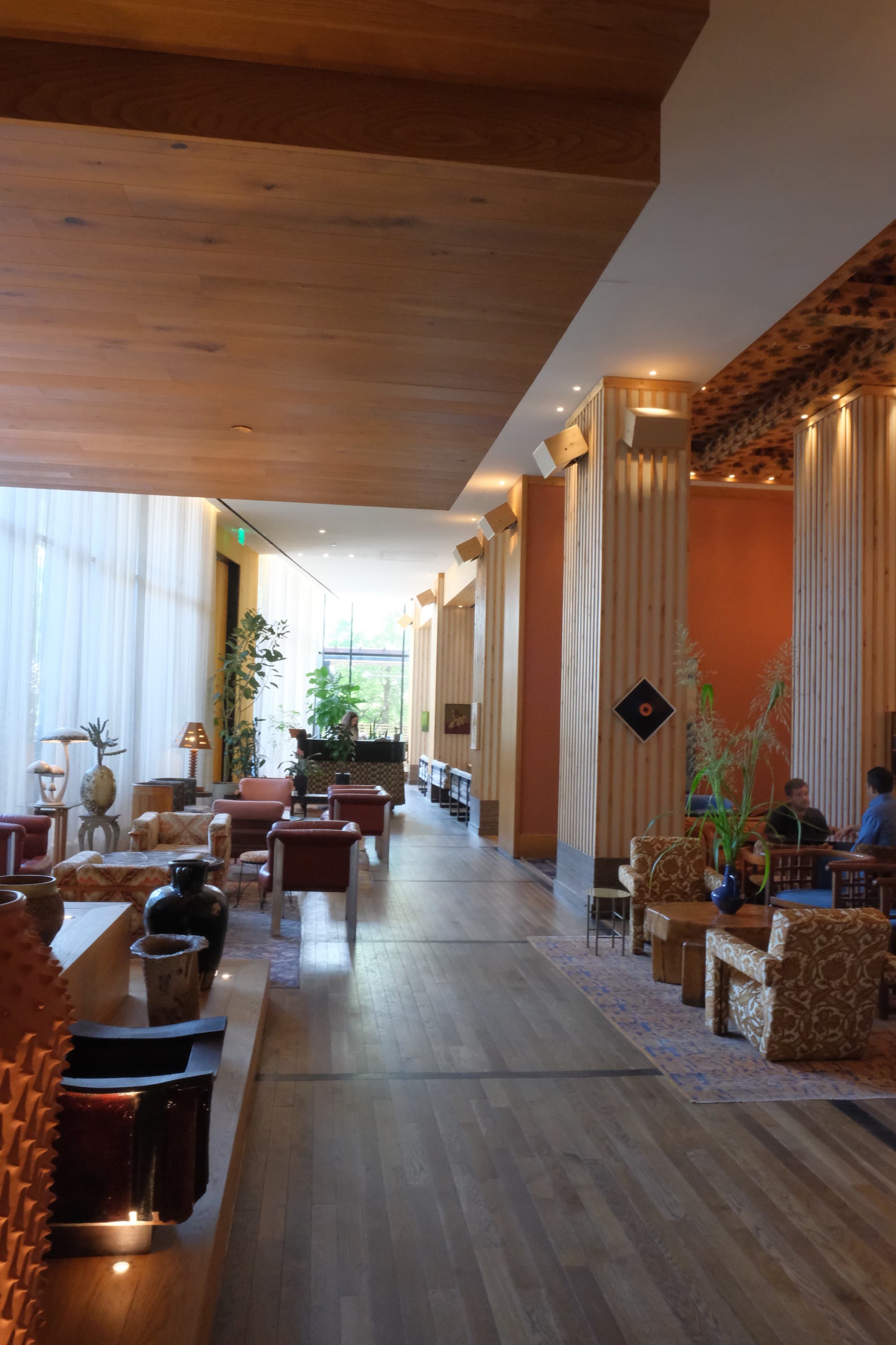 A view of the hotel lobby leading up to The Peacock lined with seating and low lighting on wooden colums.