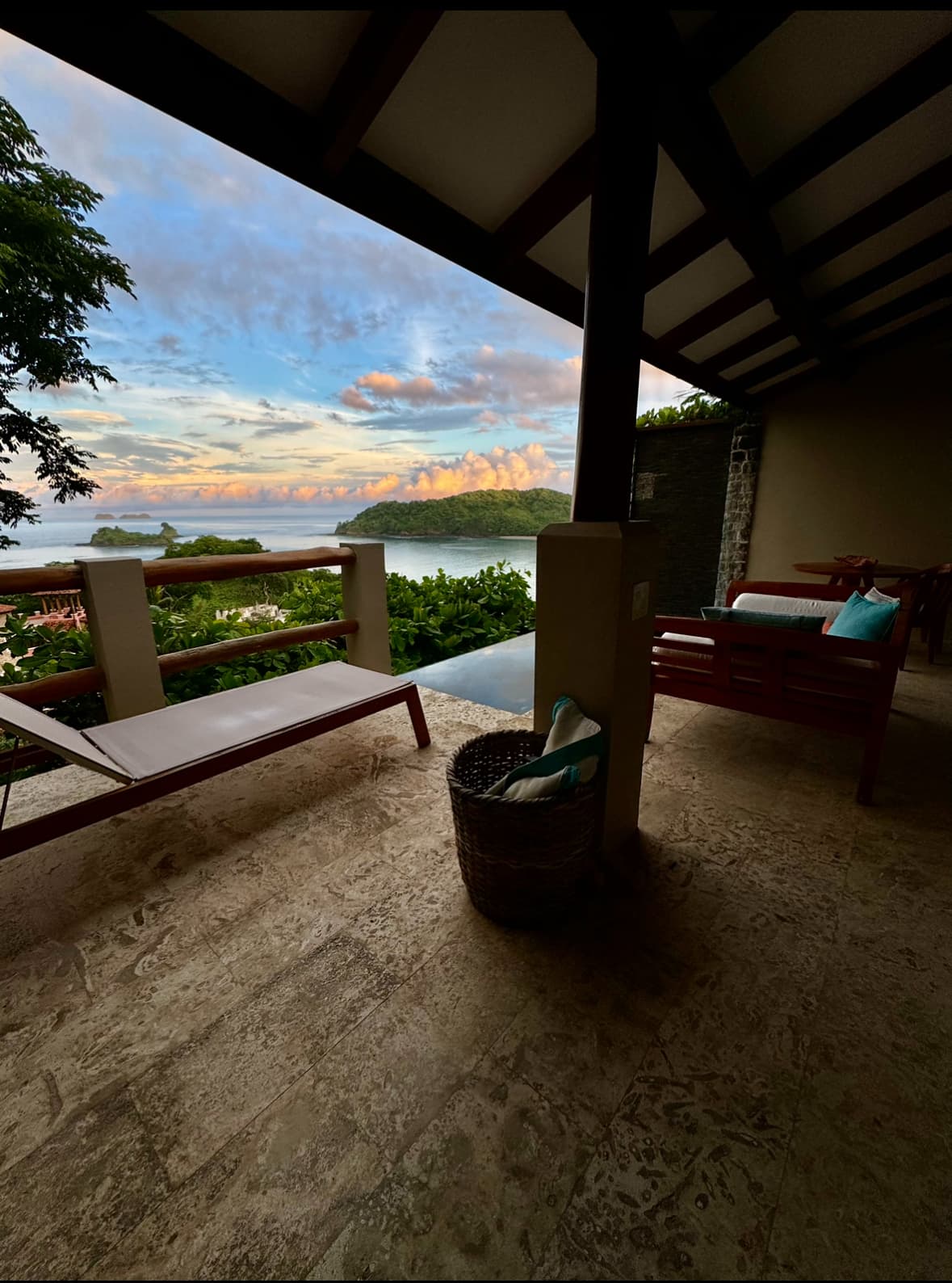 A private terrace with loungers near a private pool overlooking the sea surrounded by lush greenery at dusk.