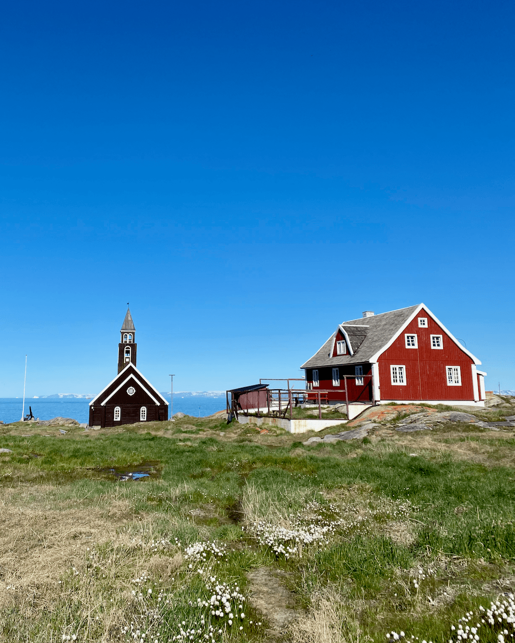 A typical red cabin and church on a grassy area overlooking the ocean in Ilulissat, Greenland