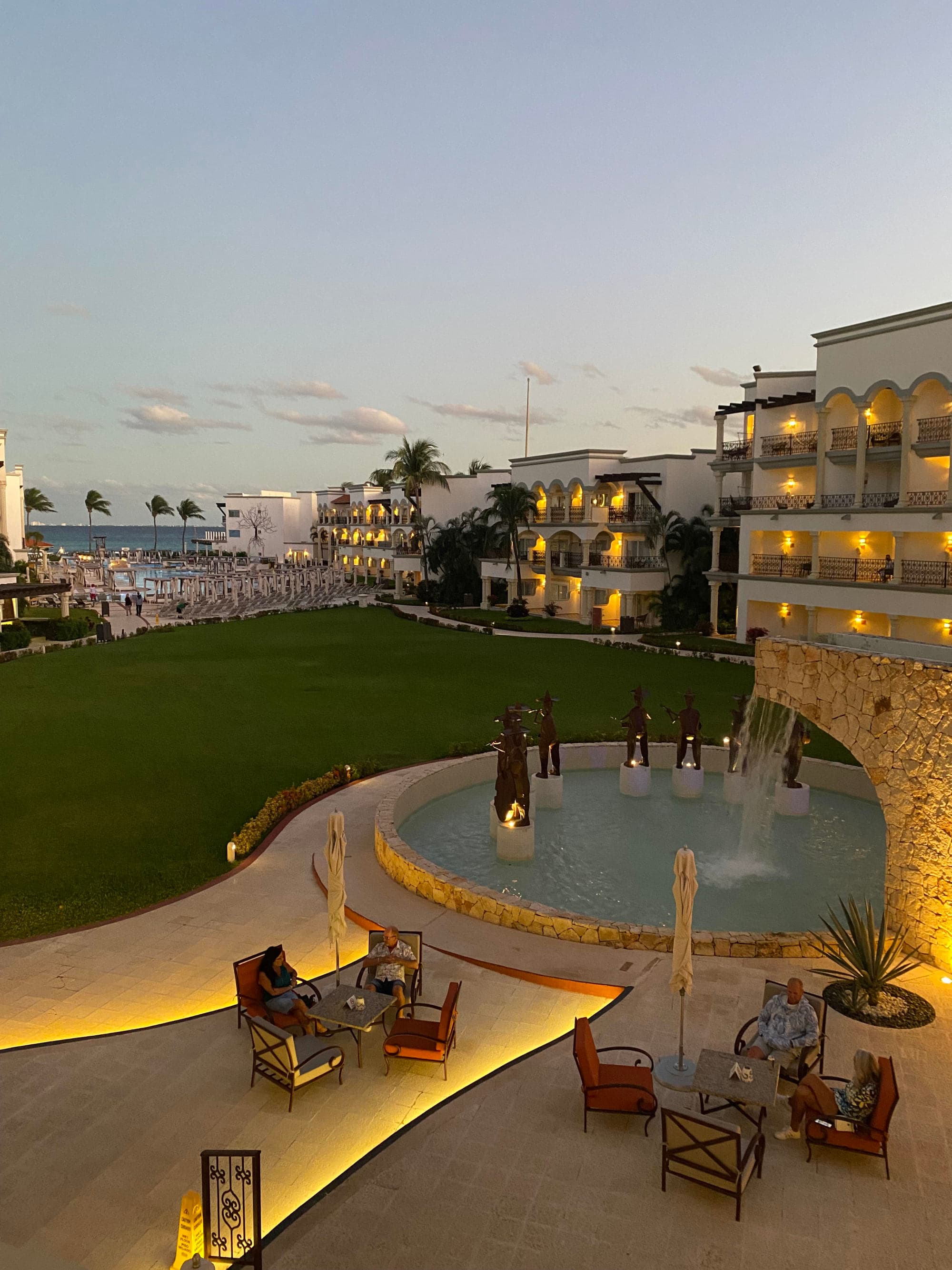 An outdoor water fountain in front of a green lawn during the evening