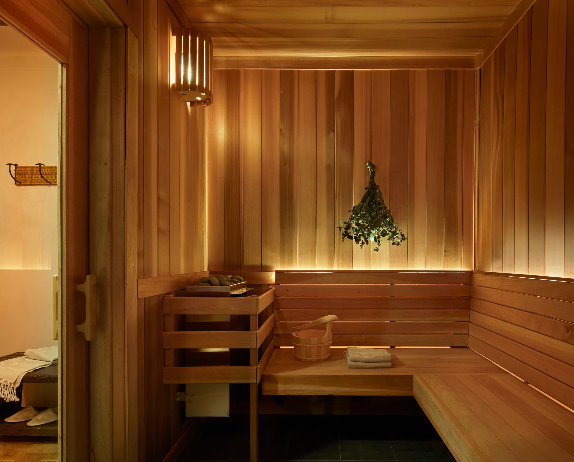 a bundle of green branches hangs in a sleek wooden sauna