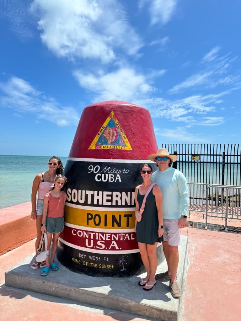 A family posing for a photo next to a monument reading "southern point - continental USA"