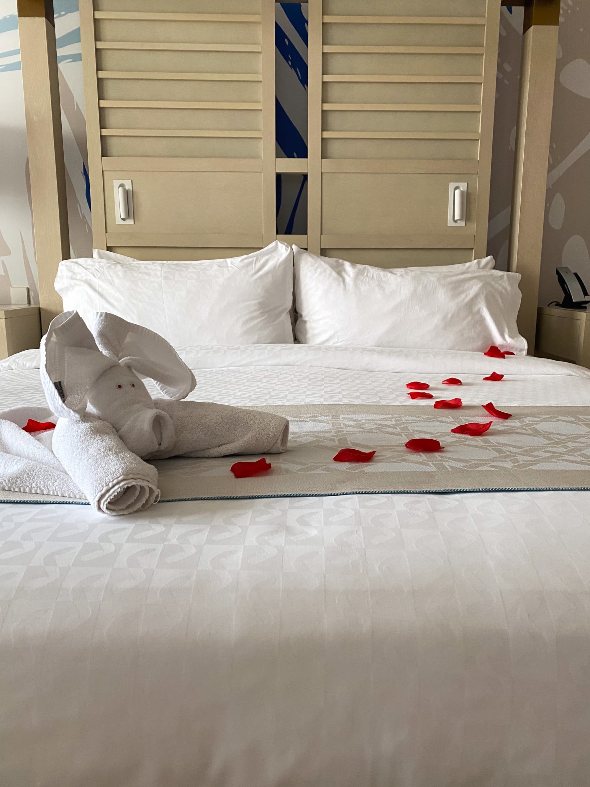 Hotel bed with white linens and rose petals.