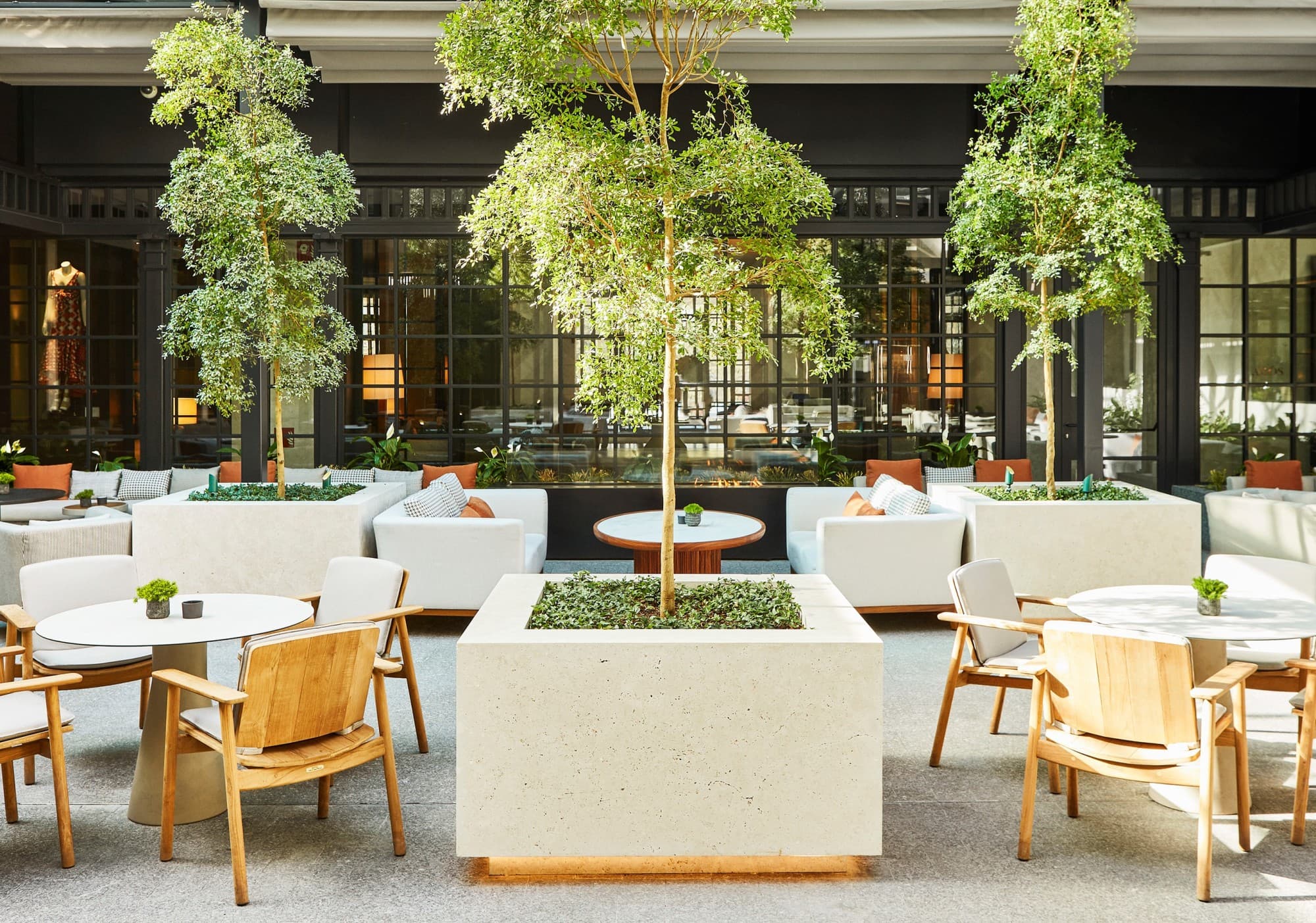 an outdoor terrace with white tables, wooden chairs, and lots of green plants