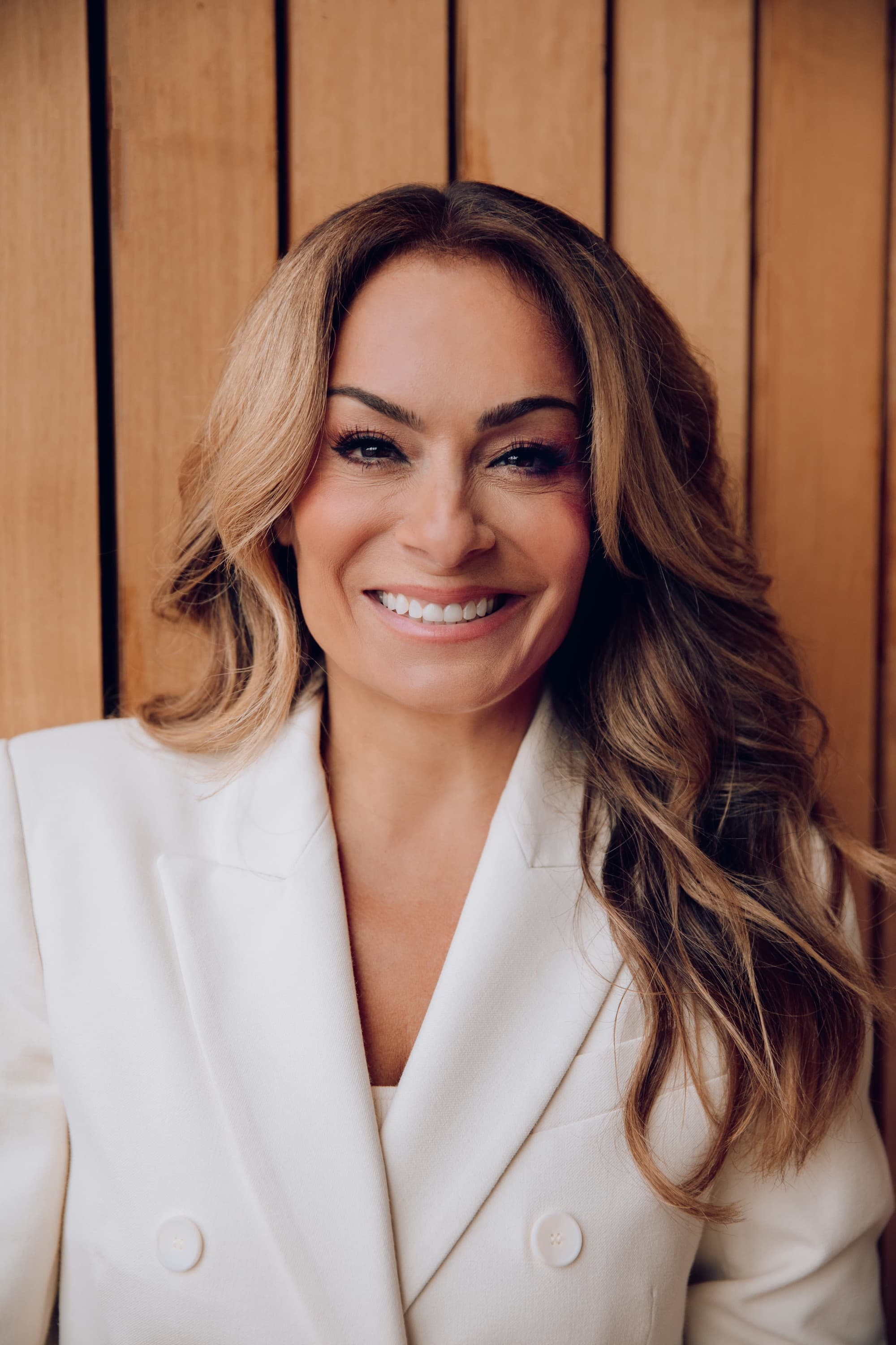 headshot of a woman in a white blazer with long brown hair smiling at camera