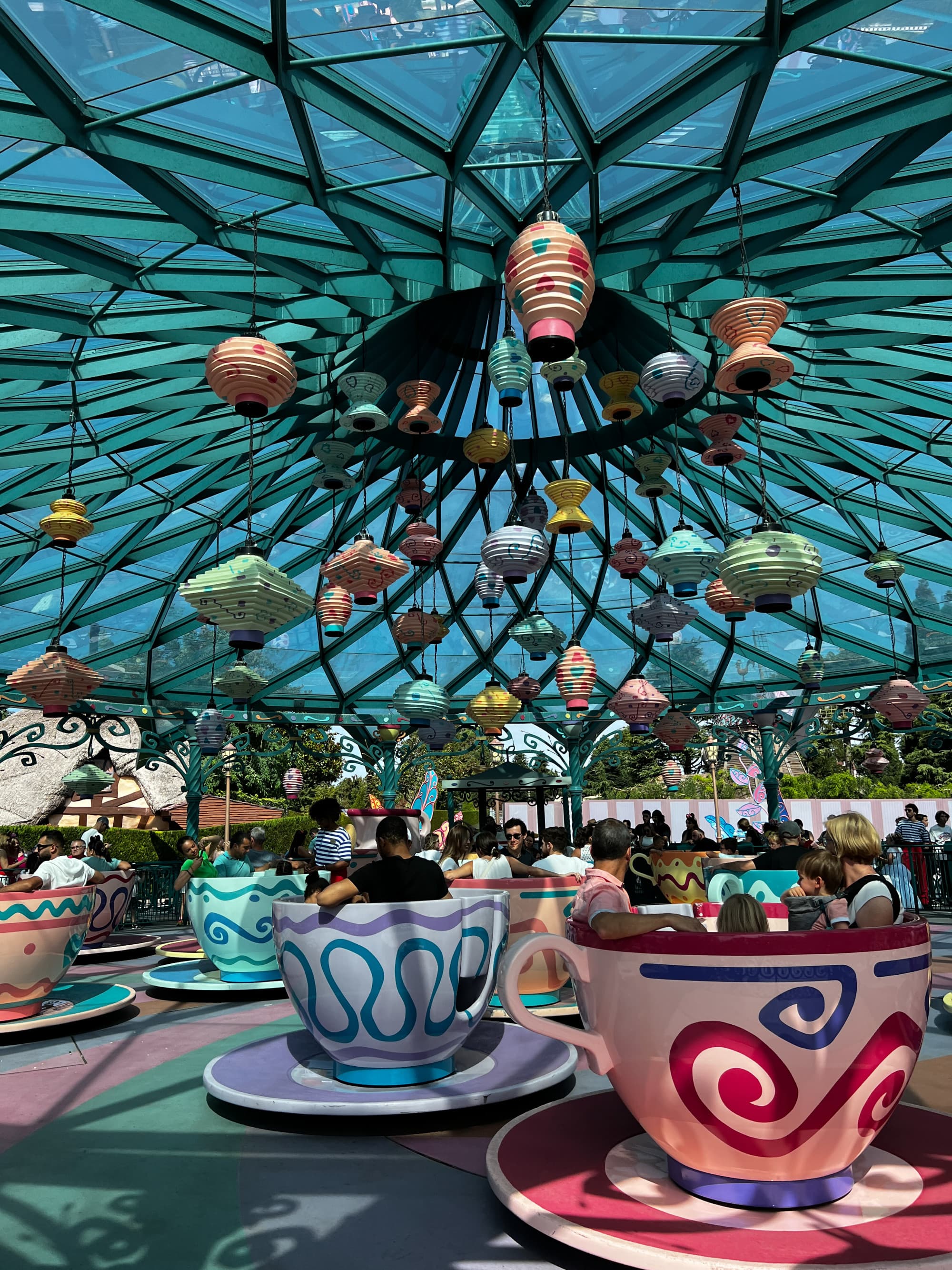 Disneyland Paris theme park ride with tourists spinning in giant tea cups under a glass canopy.