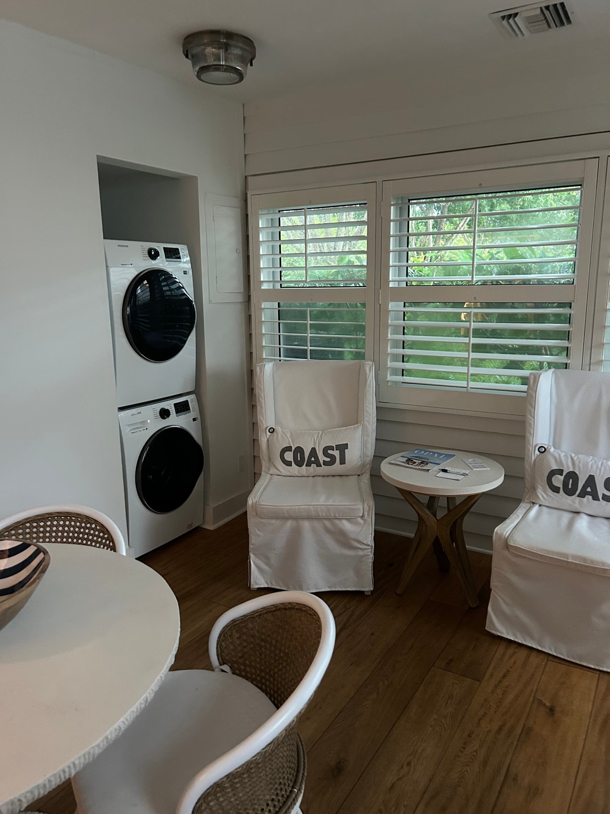 Hotel suite with white chairs in front of a window and a washer and dryer unit.