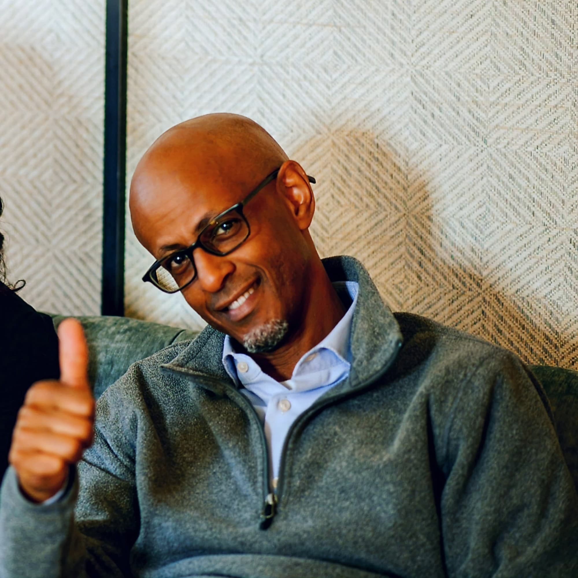 man in a gray sweater looking at the camera giving a thumb's up