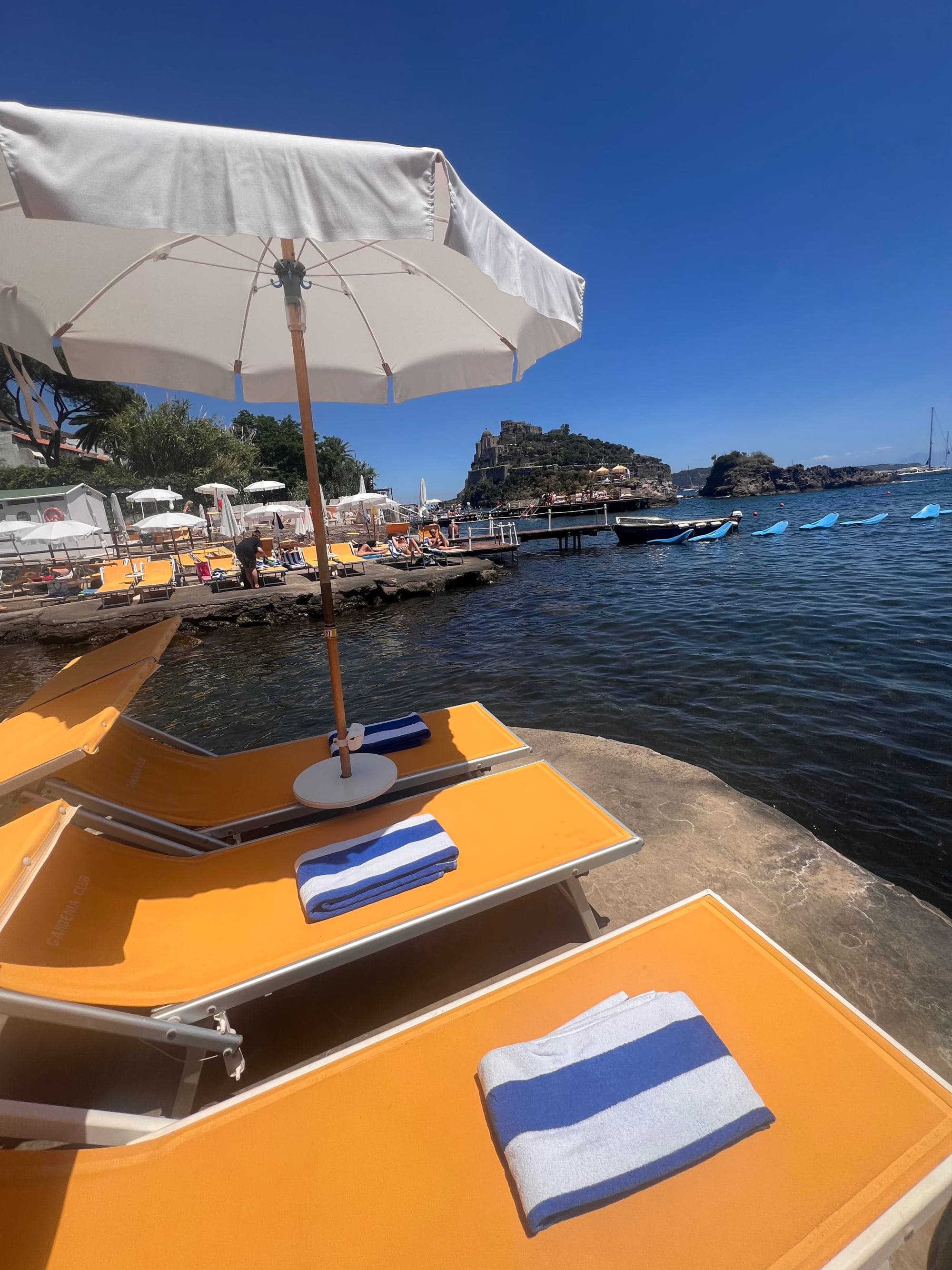 A view of yellow chaise lounge chairs under a white umbrella overlooking the ocean during the day.