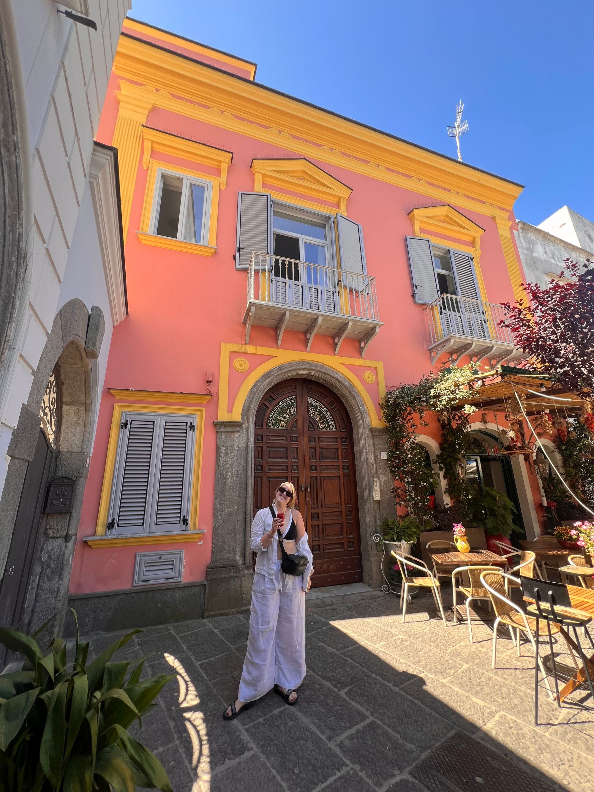 Travel advisor posing outside a pink and yellow building on a sunny day.