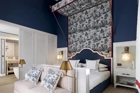 a chic blue hotel room with a bed with a patterned canopy