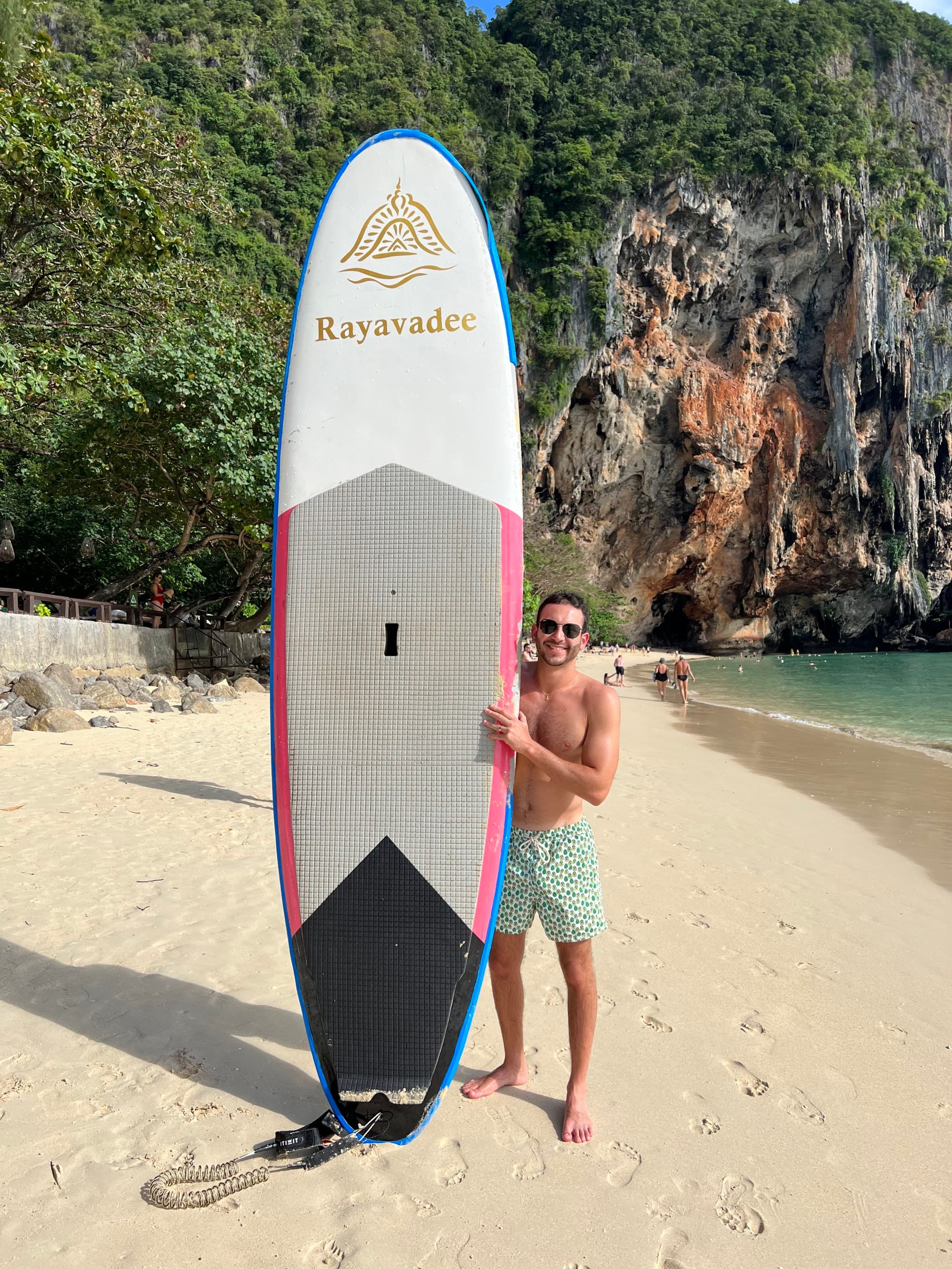 a man in blue swim trunks holds up a surfboard on the beach