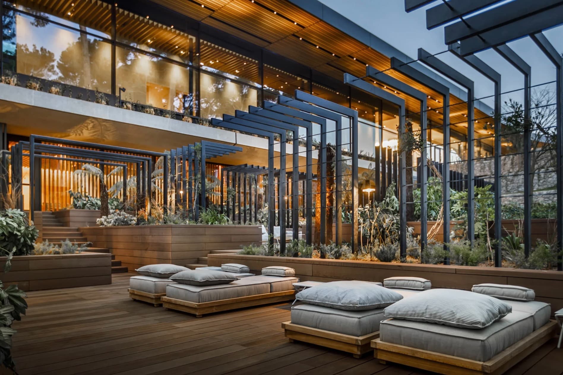 stylish outdoor terrace with cushioned day beds and sleek glass wall and greenery