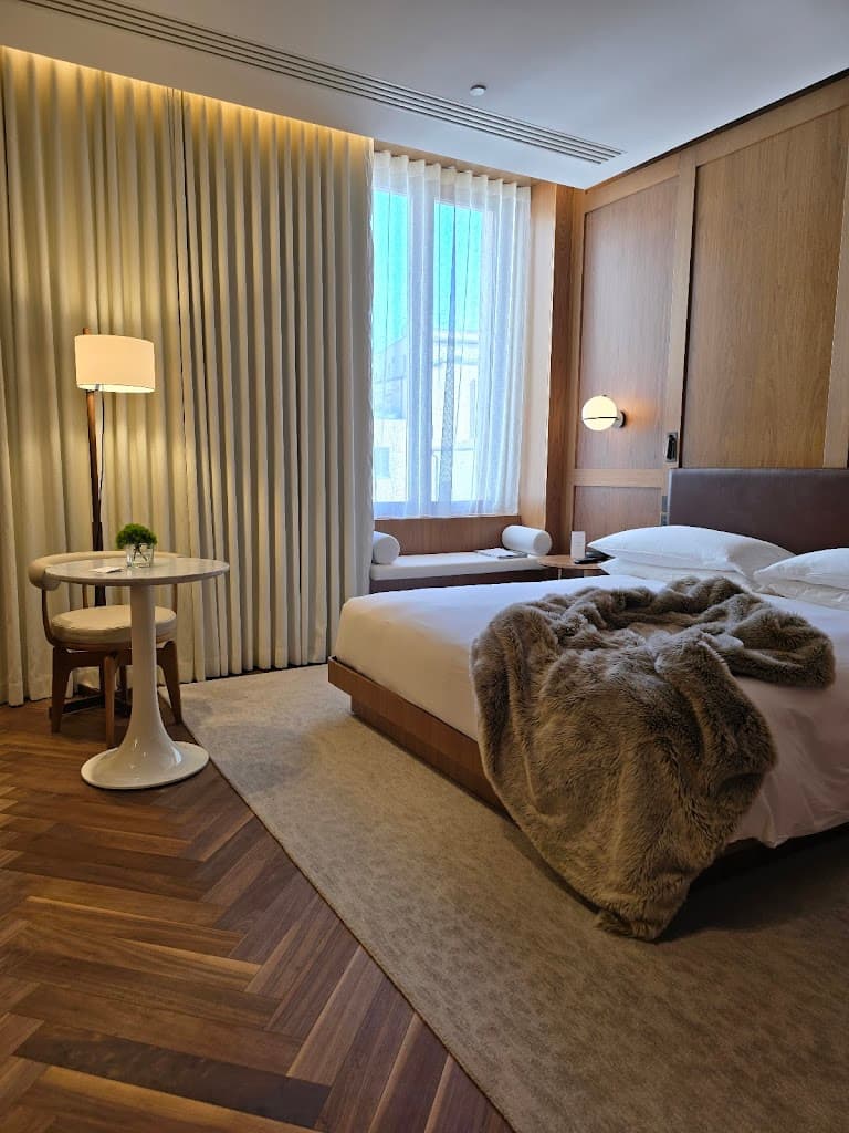A bedroom at the Rome EDITION, with a large white bed, cozy brown blanket and wood floors.
