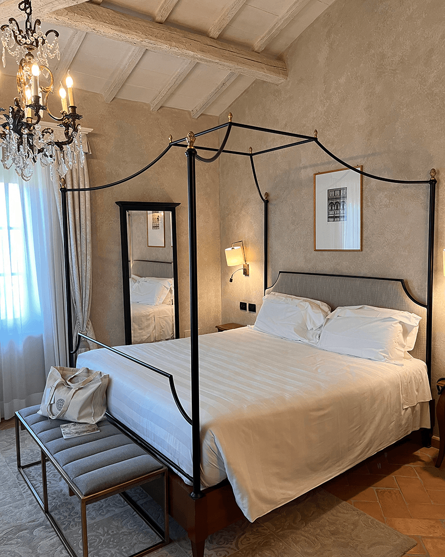 The master bedroom of the villa's Junior Suite, with a canopy style bed, chandelier, and rustic-chic decor.