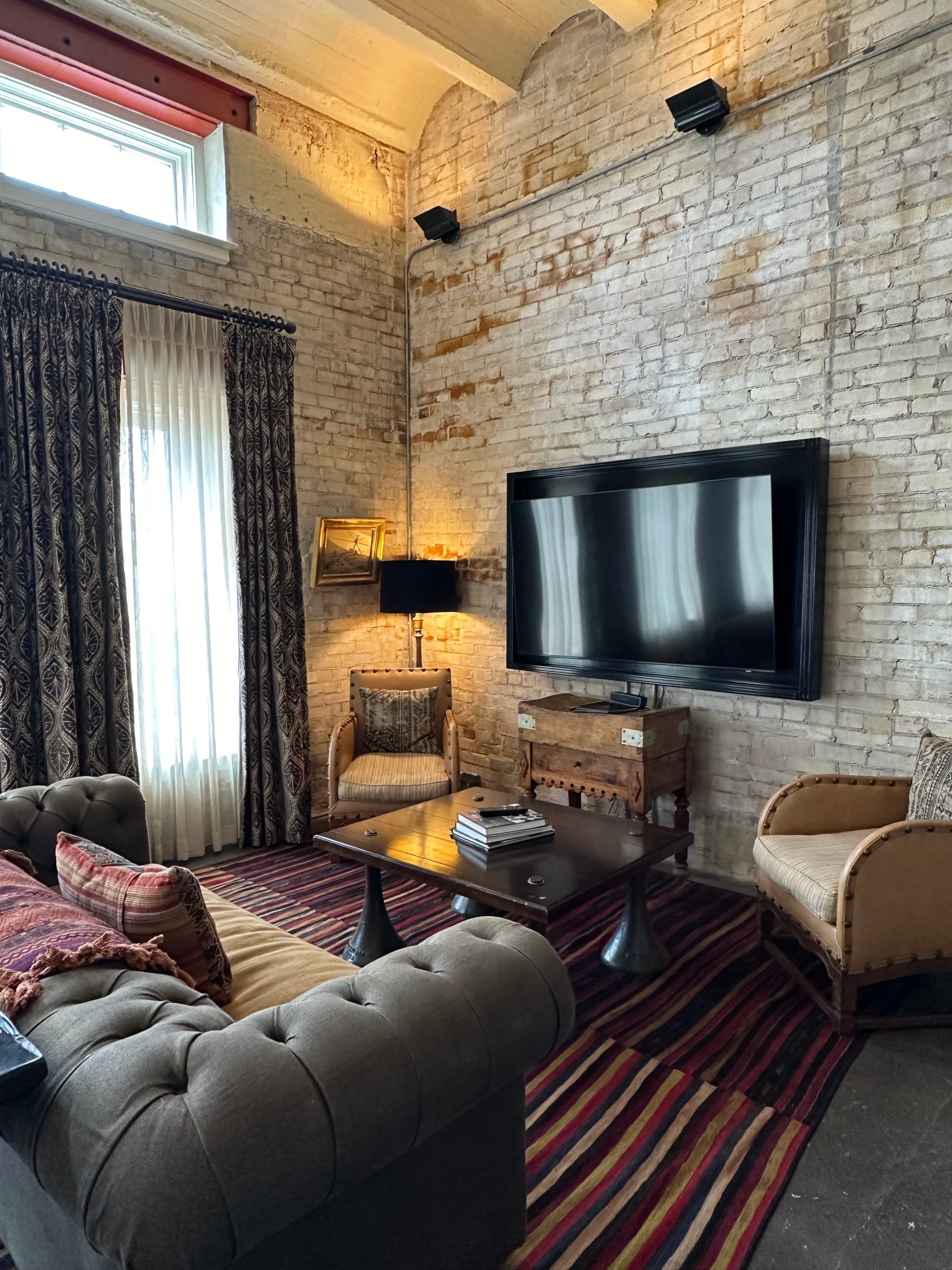 The sitting area in the suite with a leather couch, two small chairs and a TV mounted on a brick wall.