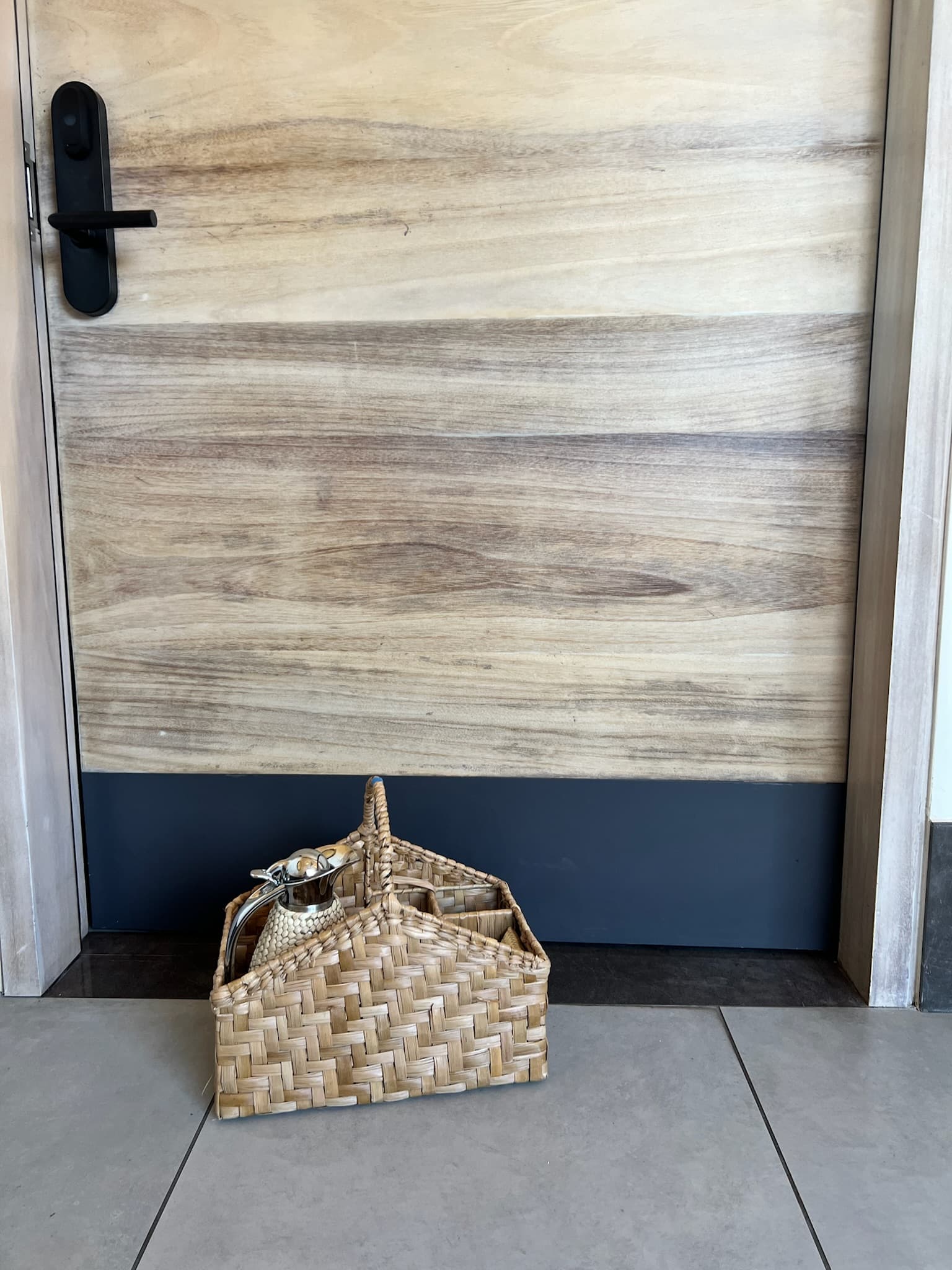 A weaved basket with a decorative tea kettle inside, with a wooden door behind it.