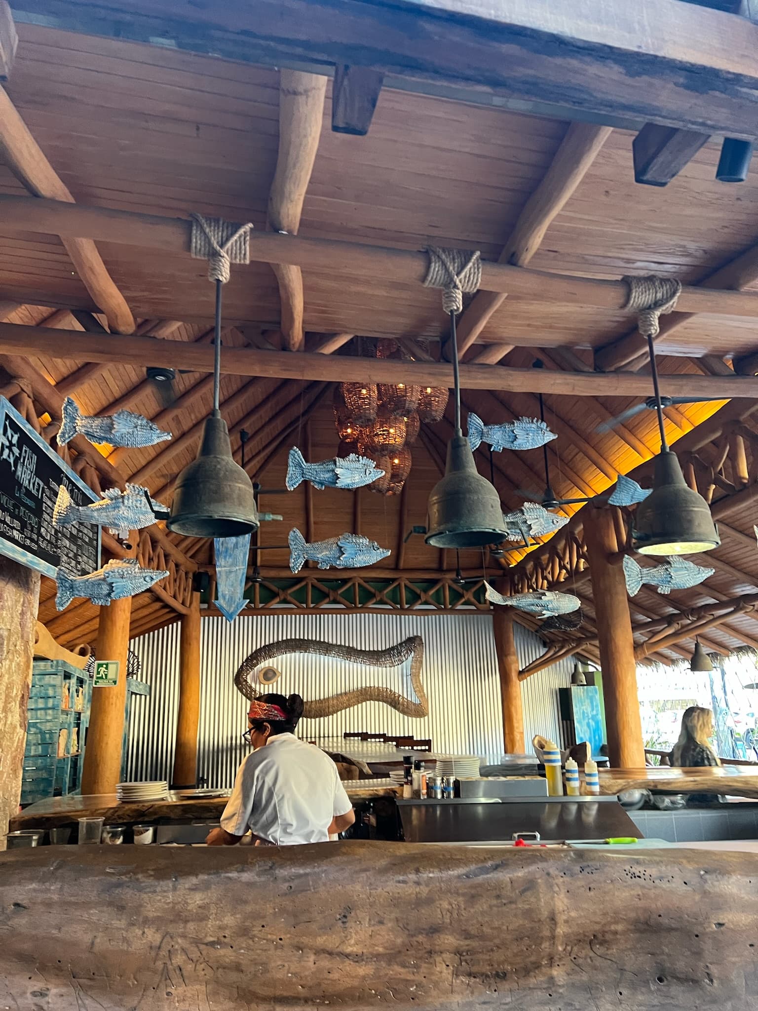 A look inside the open kitchen and staff member at La Pescadora, with decorations of hanging fish and a wooden ceiling and columns.