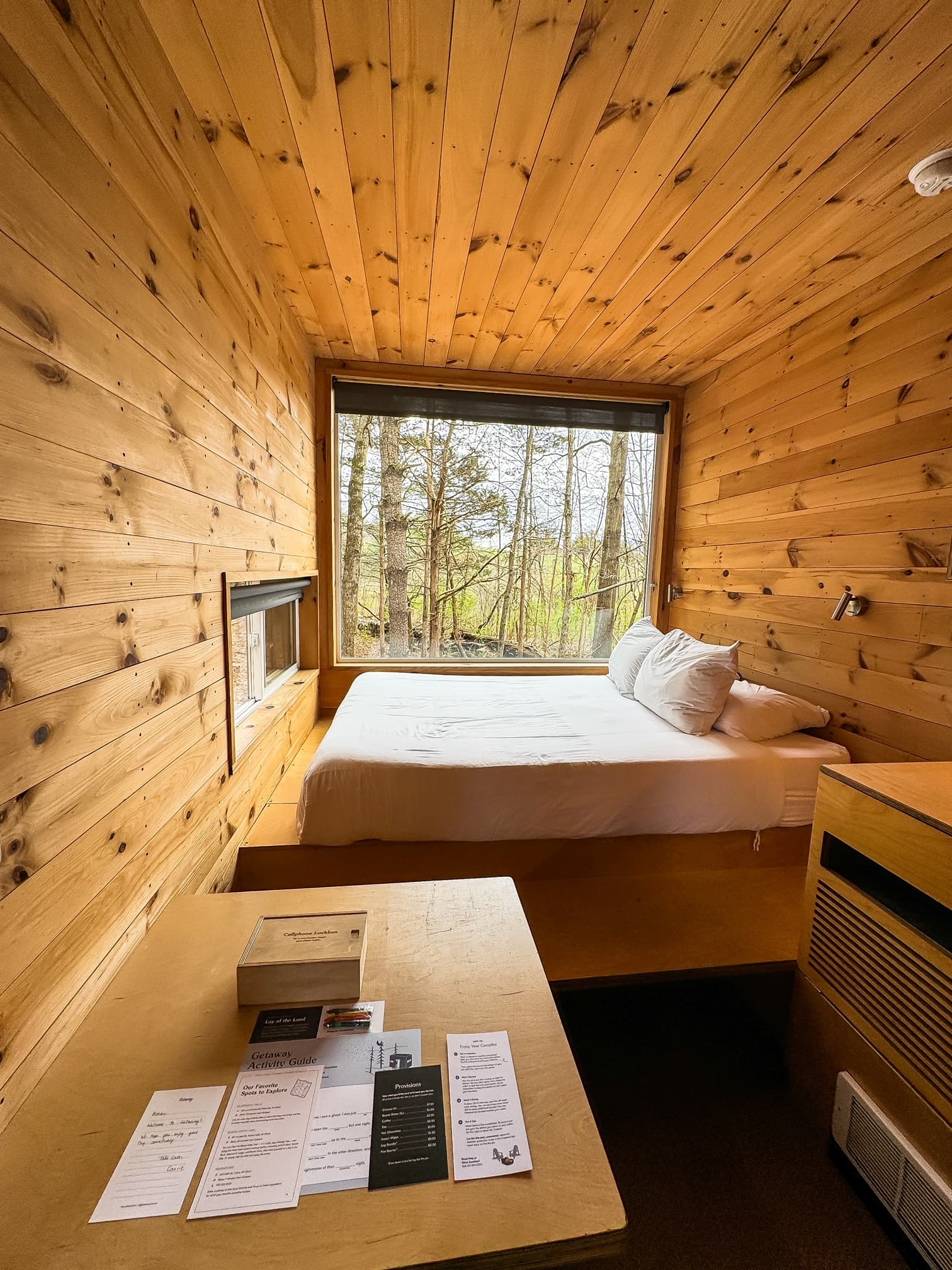 Inside of the wooden cabin, with a queen-sized bed, a desk, and windows looking out into the woods.