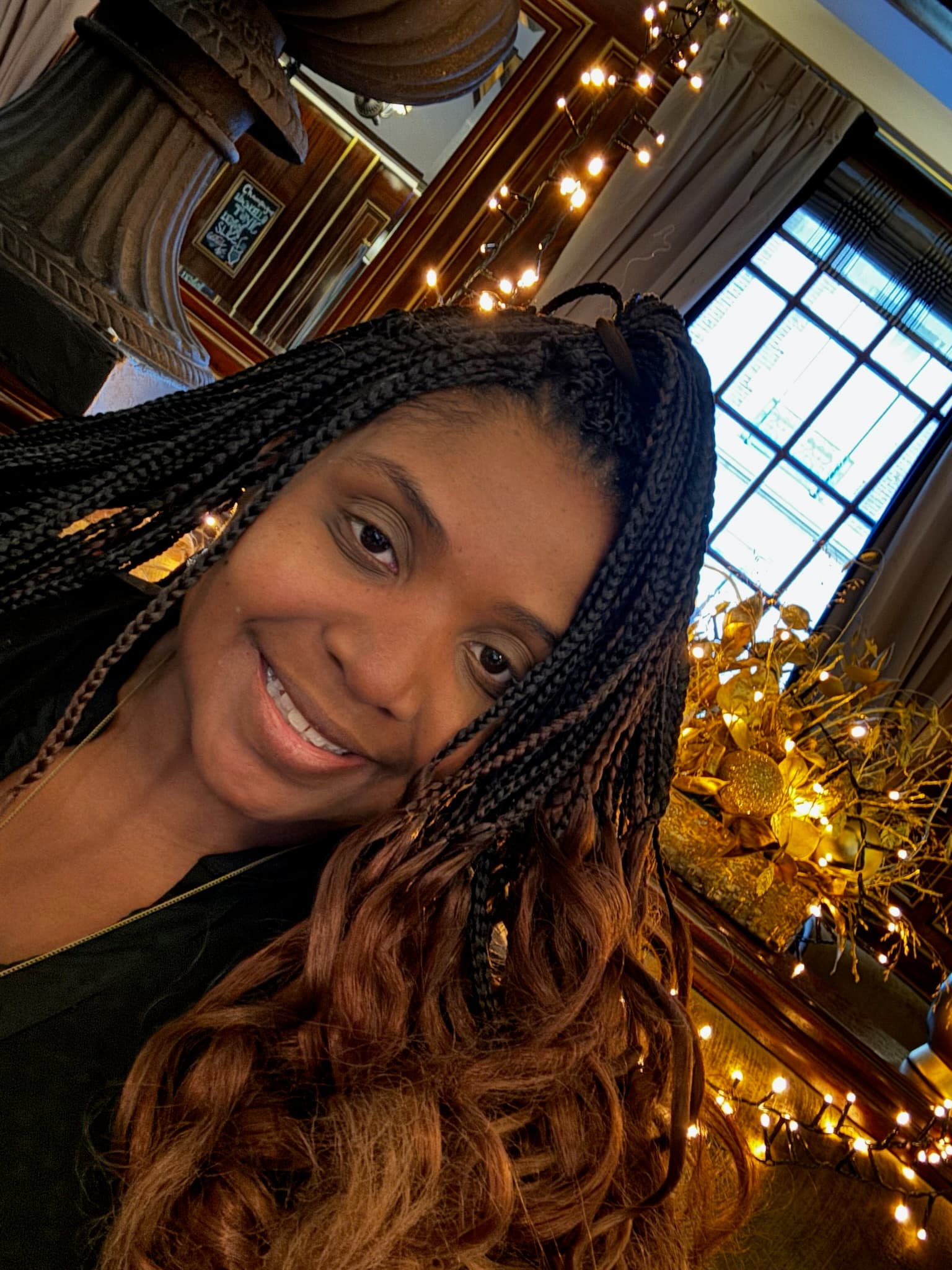 Selfie of Tysheda in a classical room with taupe curtains and fairy lights