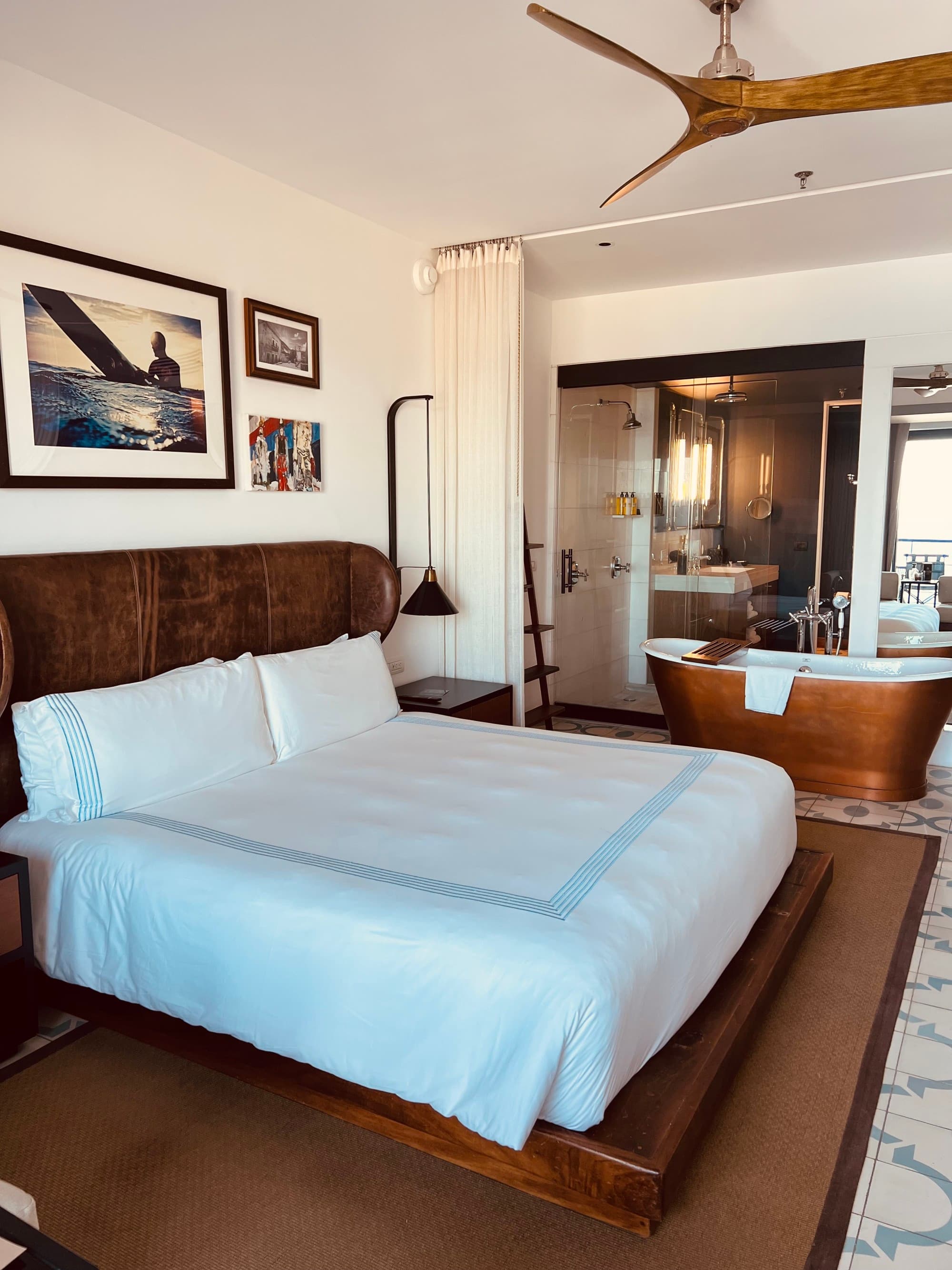 A hotel room with a copper bath tub and white bedding and wooden fixtures