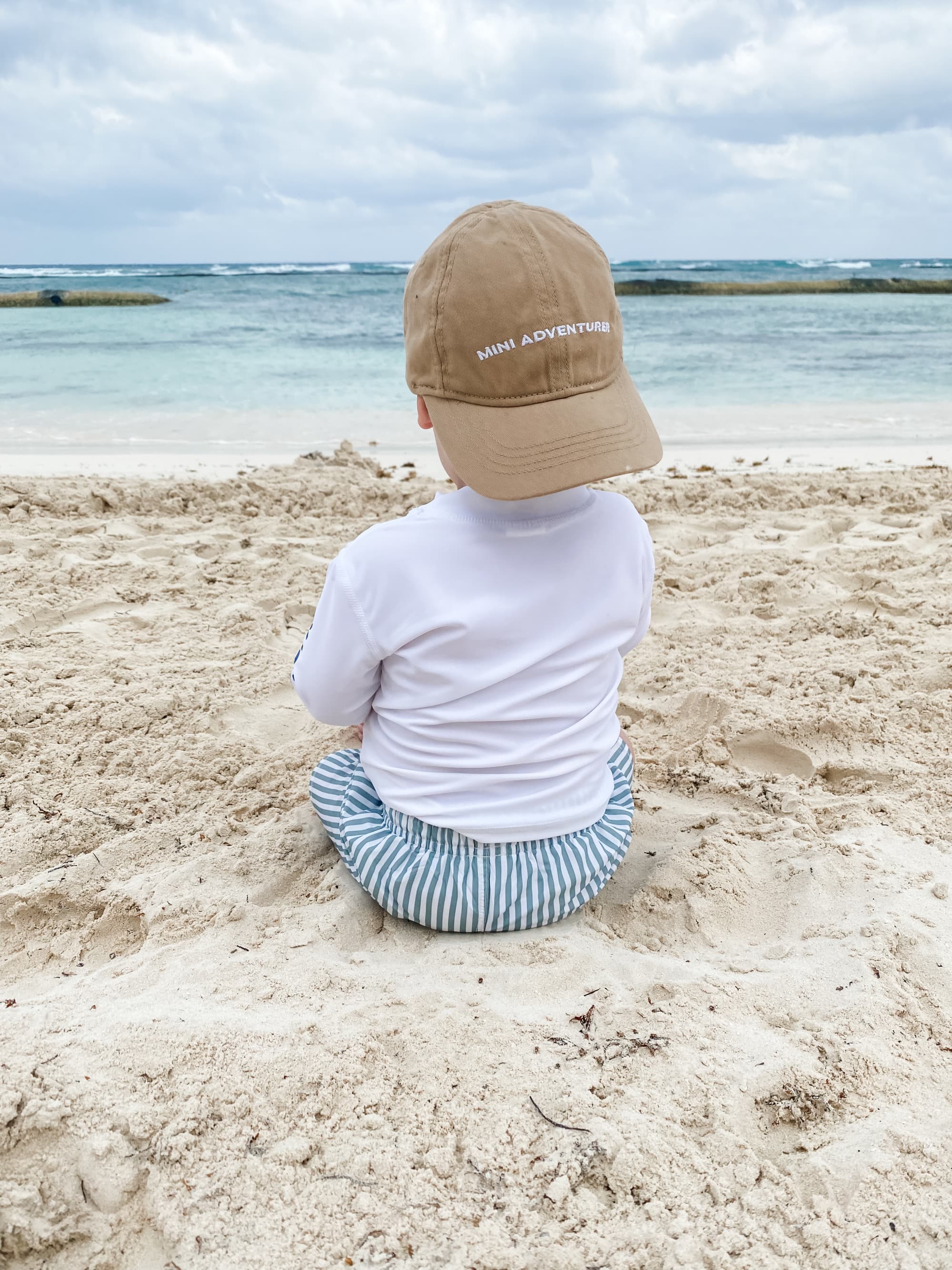 A baby sitting on the bitch with their back to the camera during the daytime