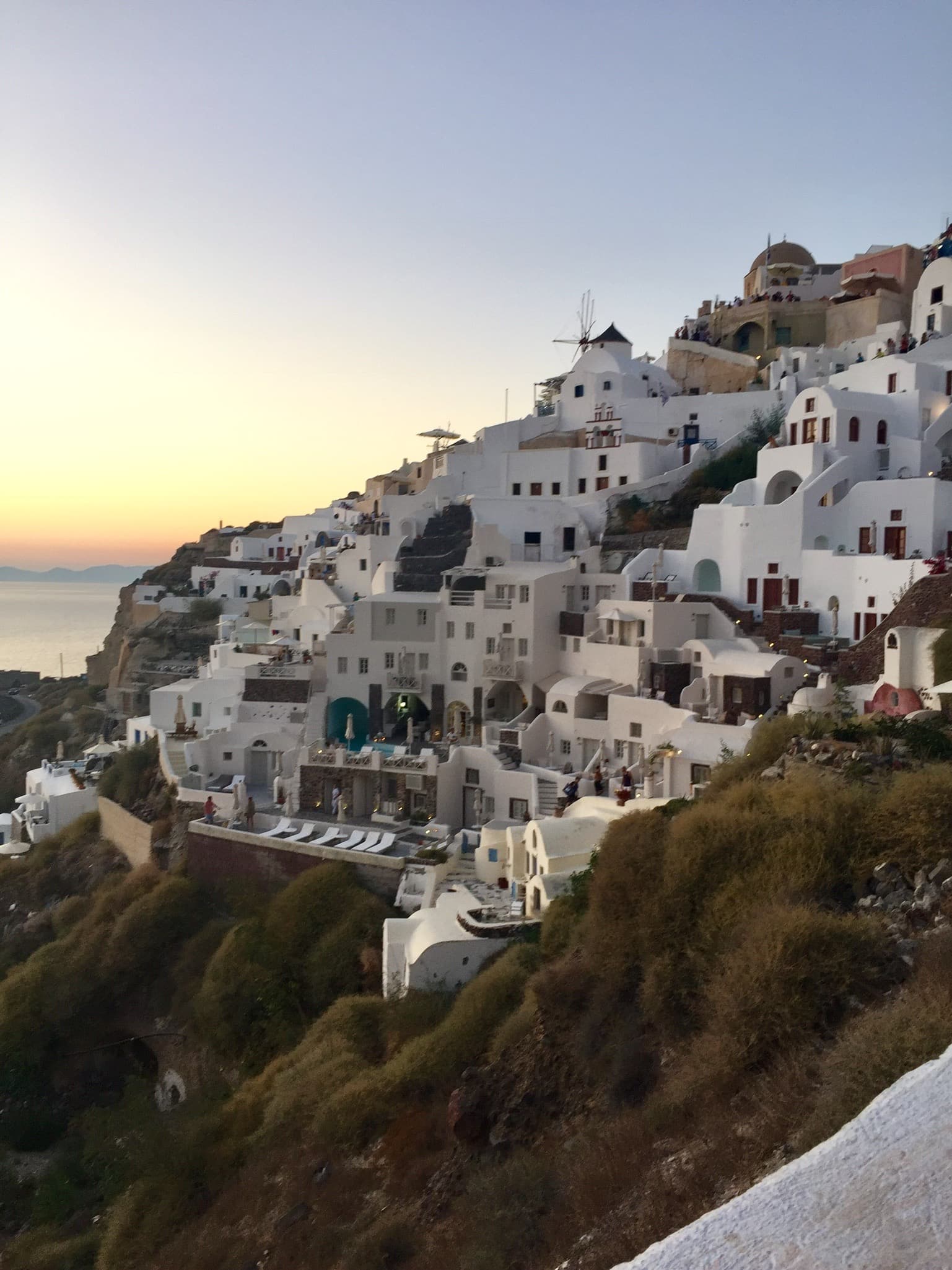 A view of the hillside with white buildings and the sun low in the sky