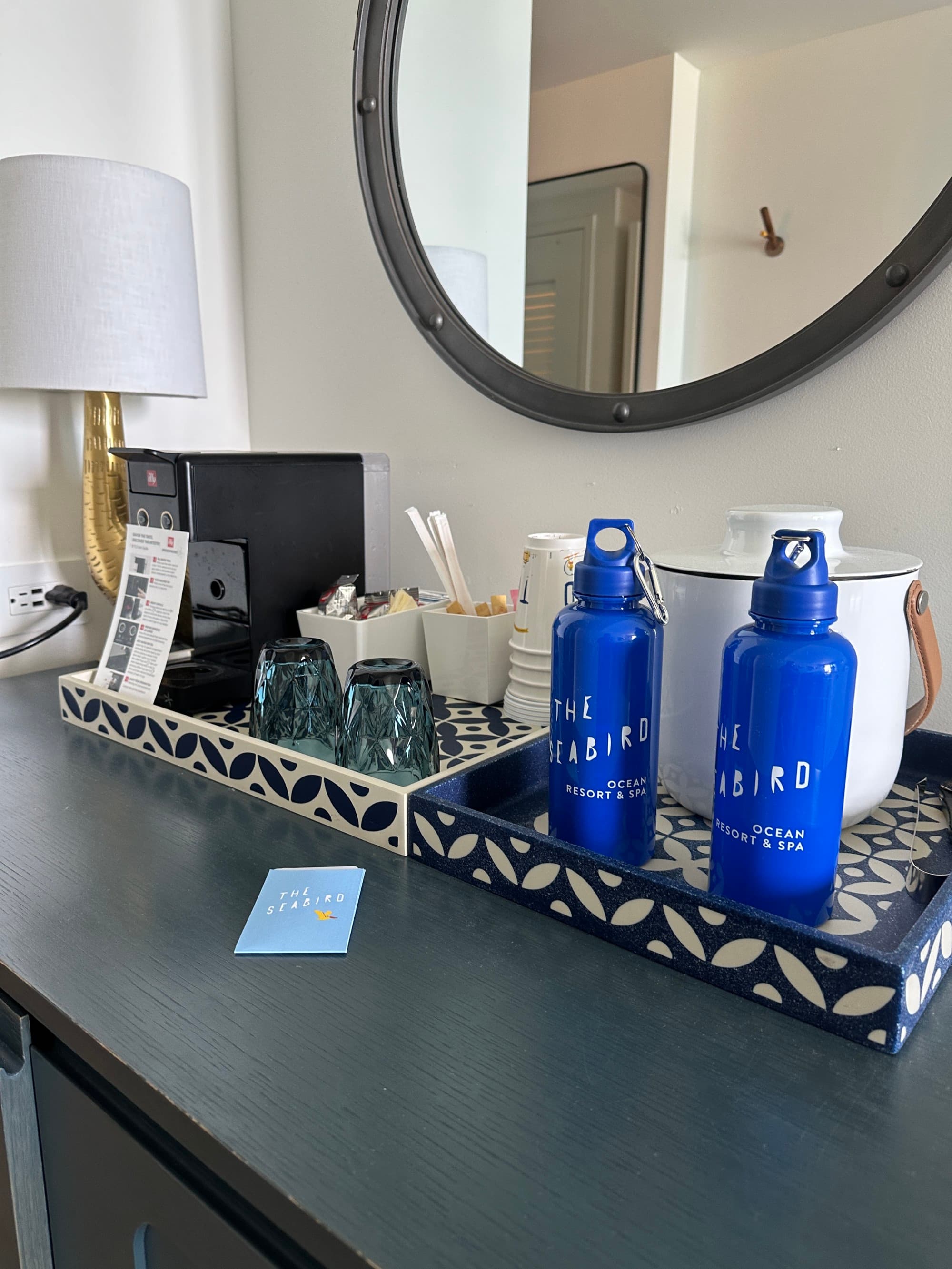 A coffee machine, cups, and water bottles on black and white trays in a hotel room