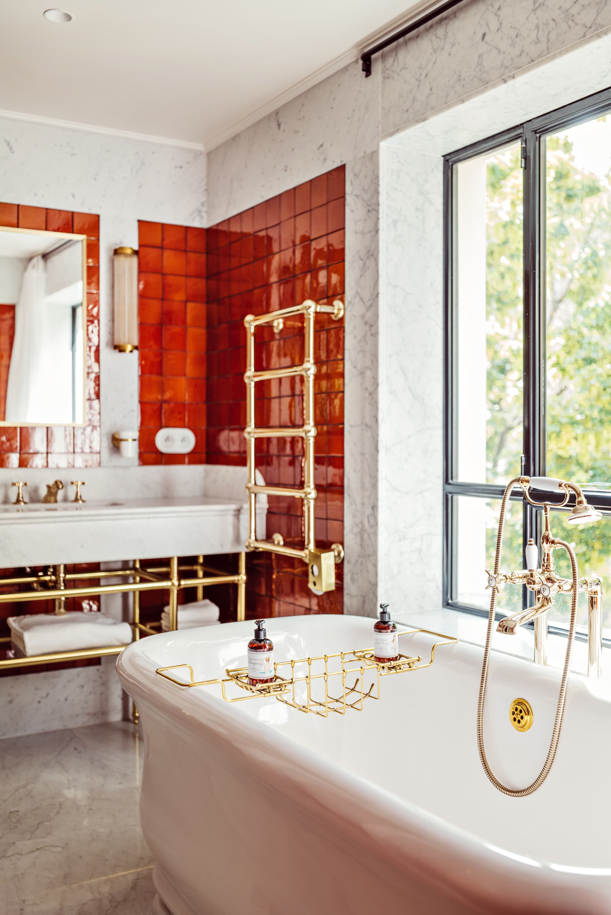 a luxe bathroom with red wall tiles and a large white tub near a big sunny window