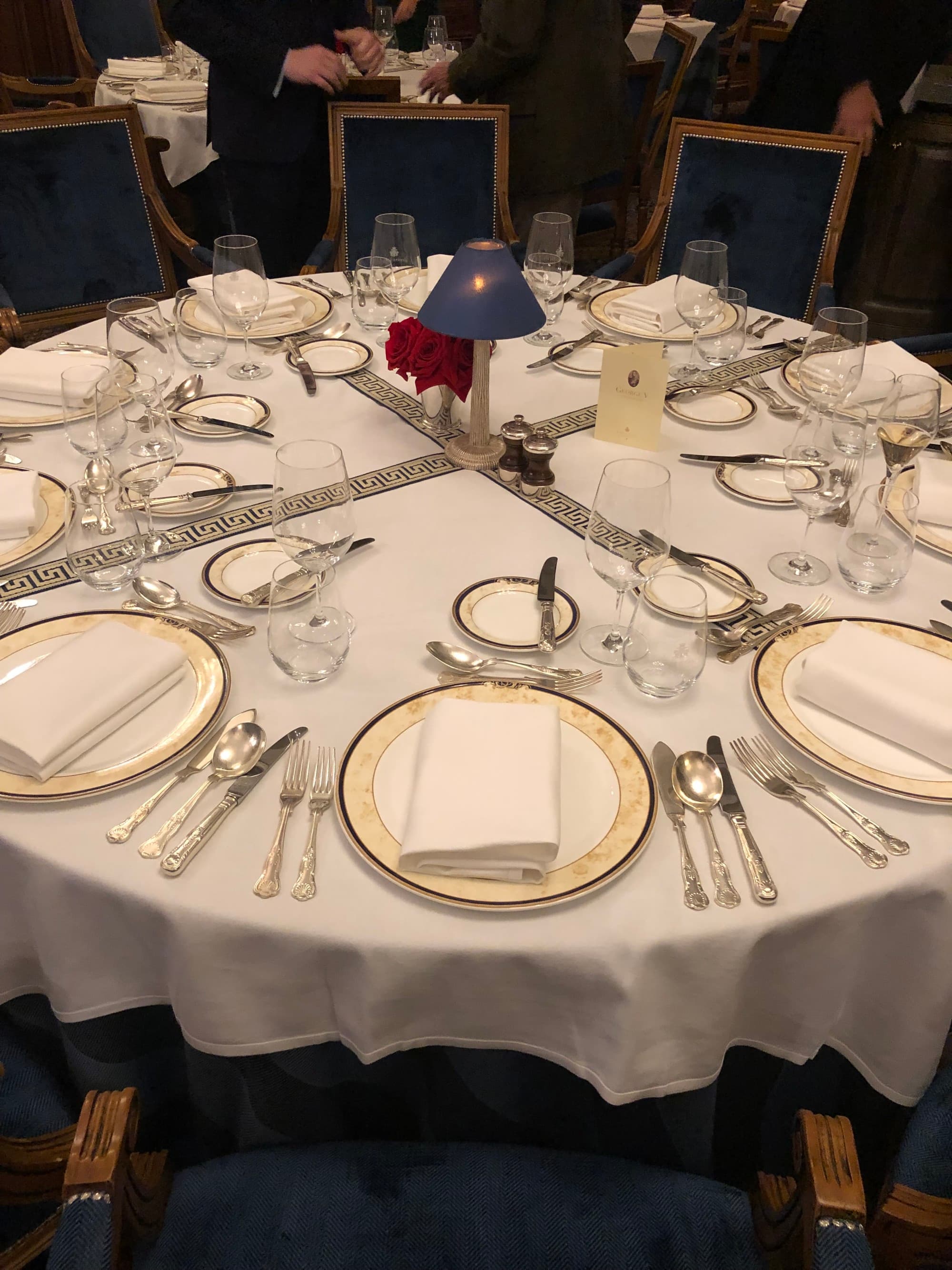 A round dining table set up with white tablecloth and silver utensils