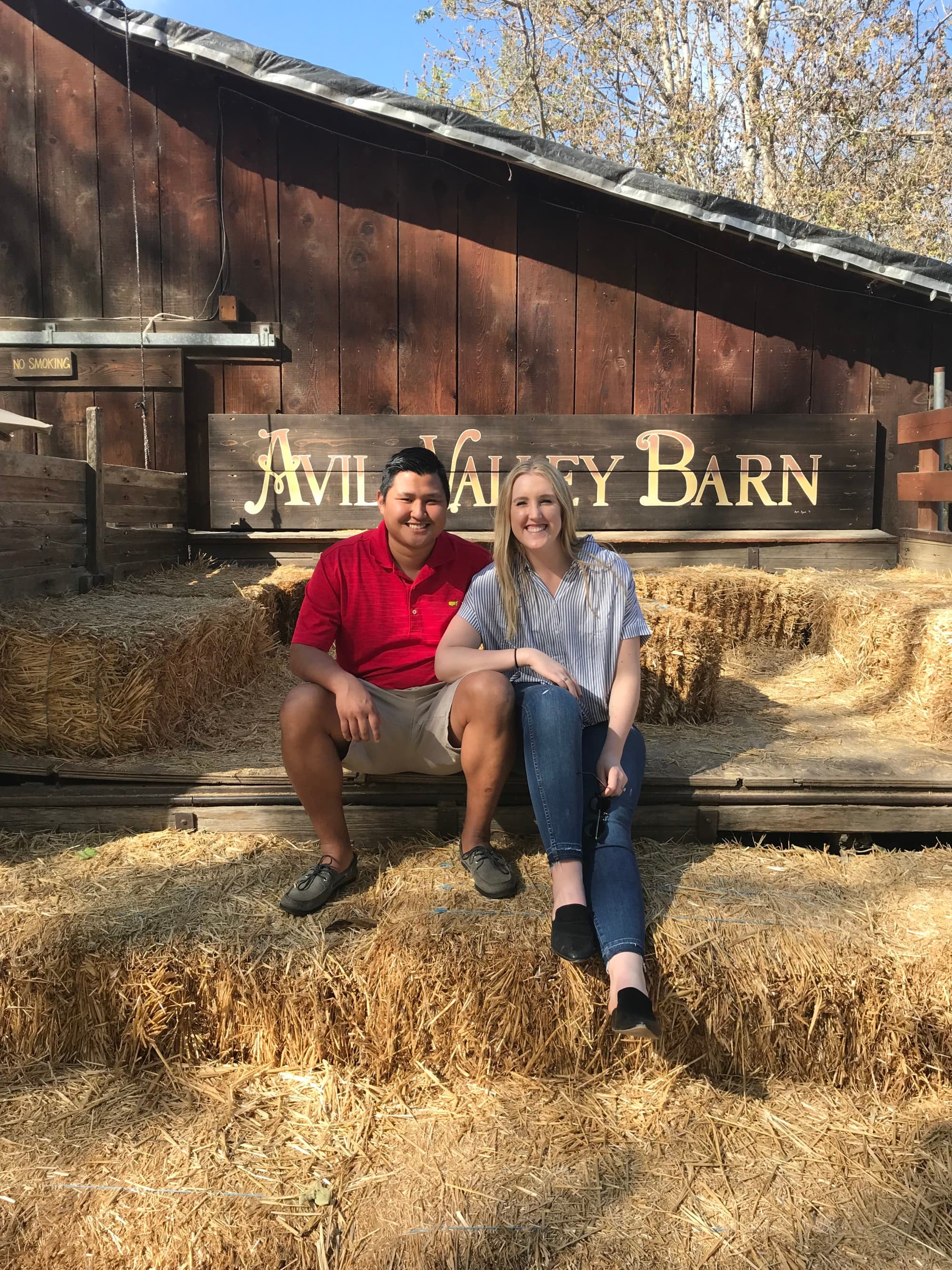 A couple posing on a seat of hay in front of a barn during the daytime