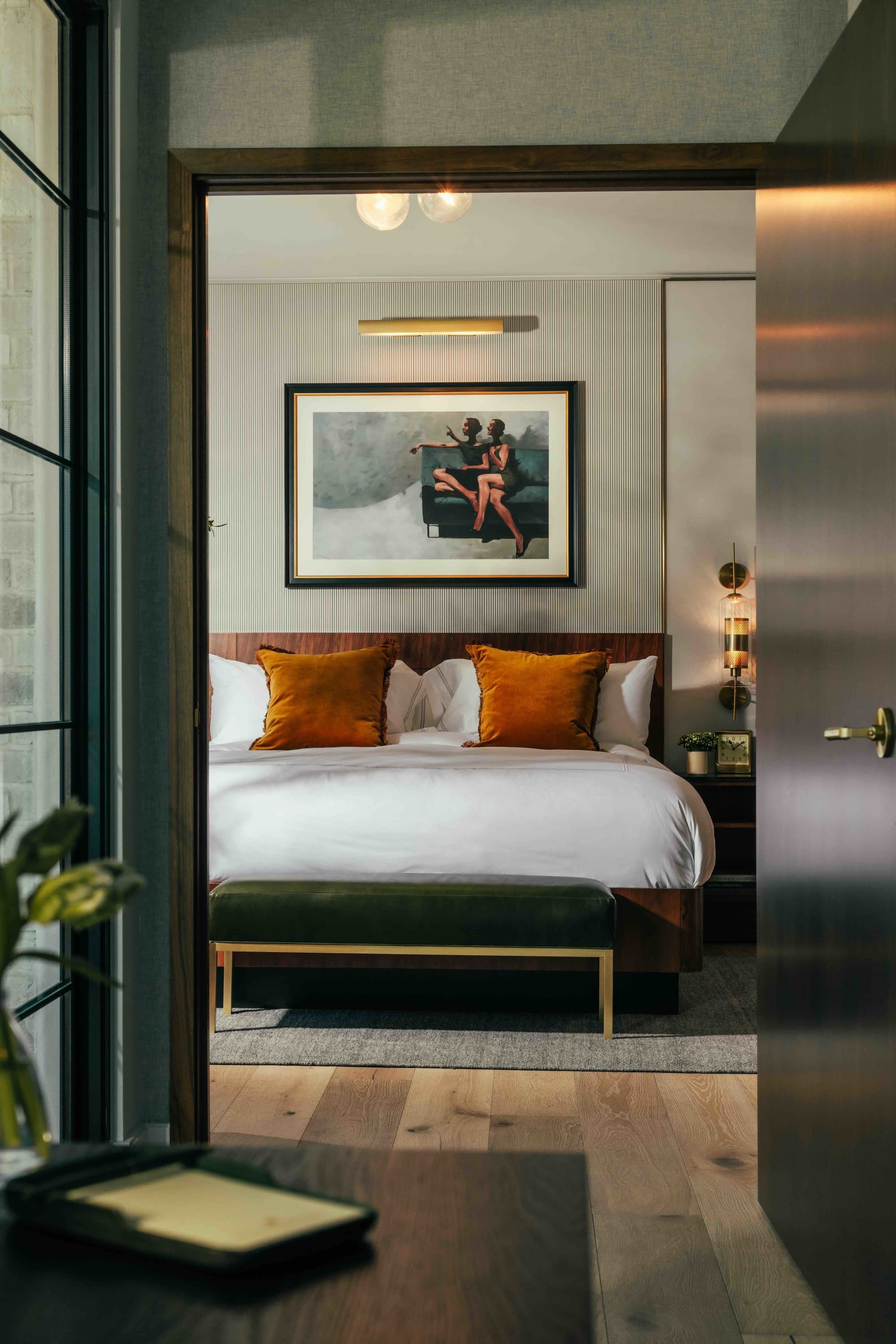 A one-bedroom suite with a white bed and orange pillows seen through a doorway from the entryway.
