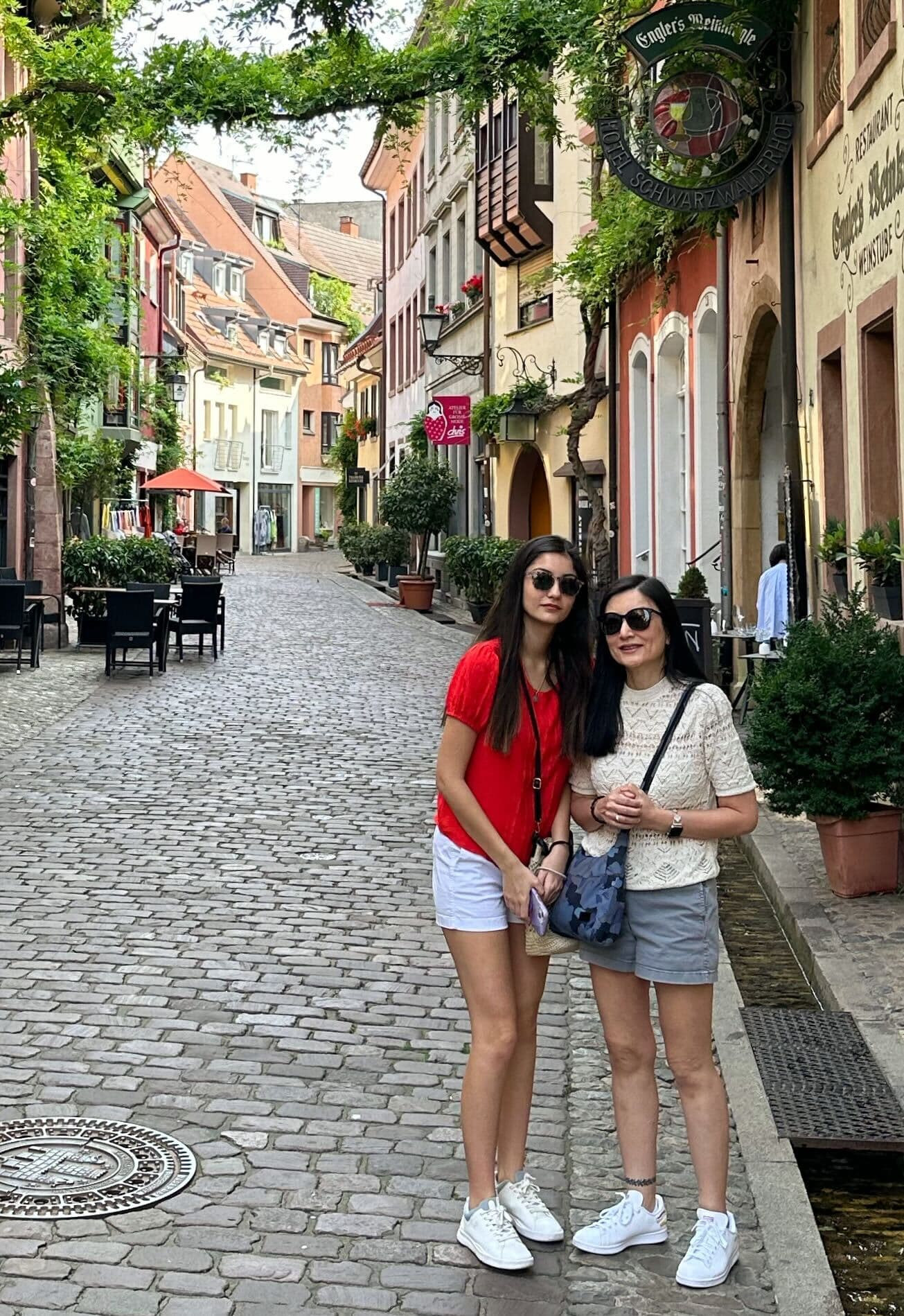 a woman and her daughter in shorts stand together in a cobblestoned alleyway