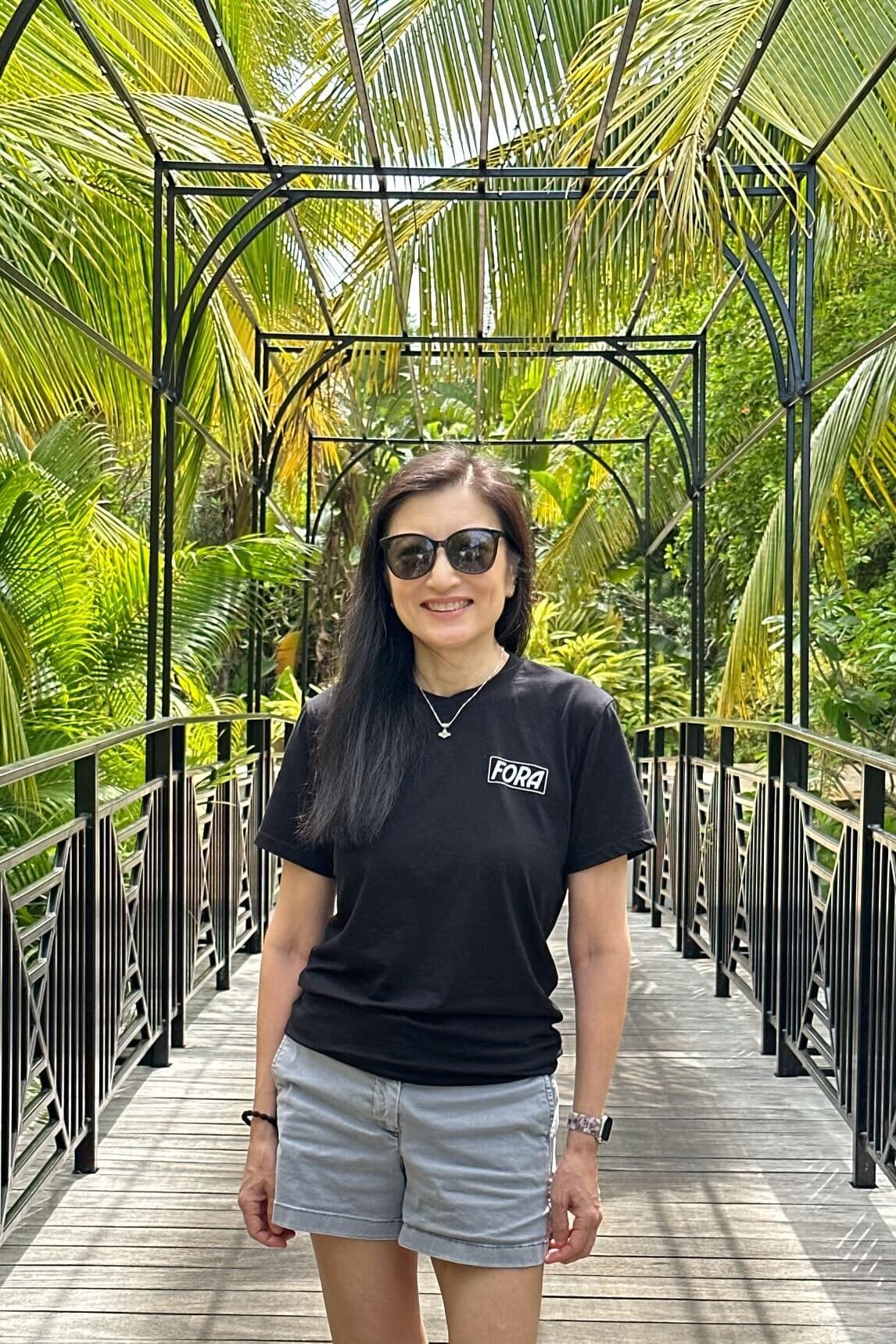 a woman in a black tee shirt and sunglasses stand in a green leafy atrium