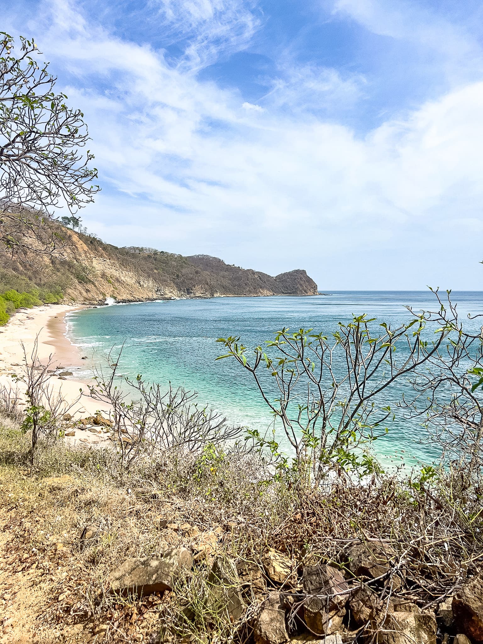 A view of the coastline of Rancho Santana Playa Rosada, with turquoise-colored water, mountains and fauna.